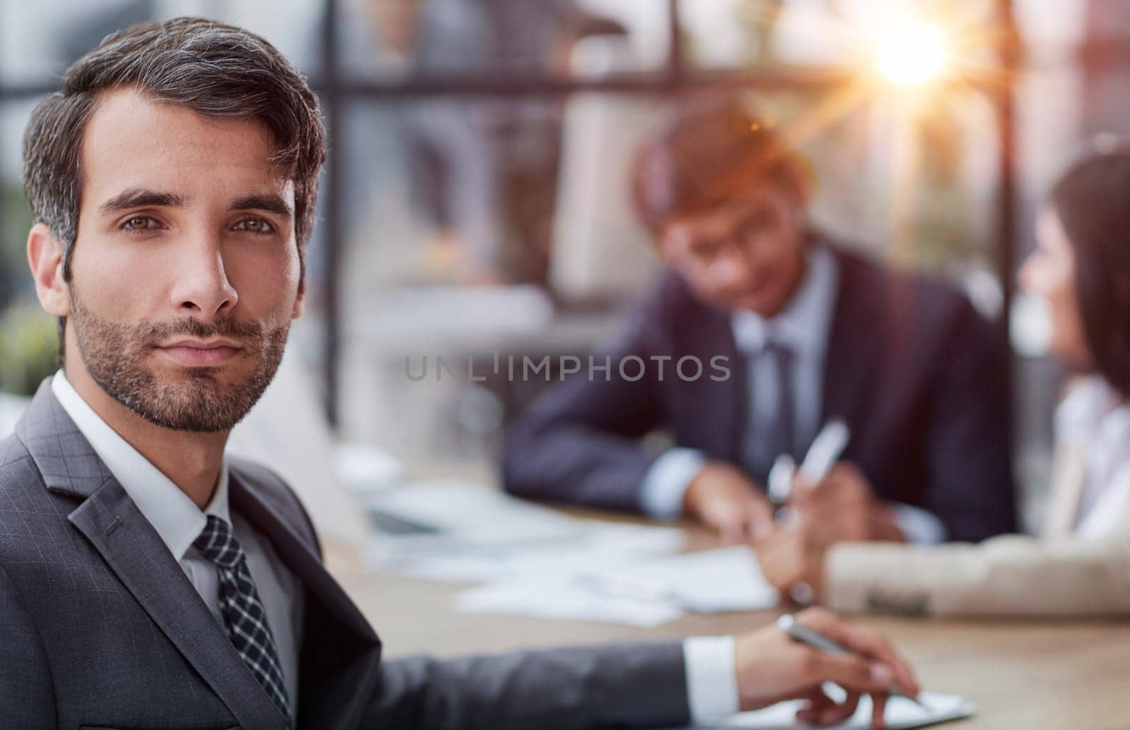 young man posing for the camera while sitting at a table in the office against the background of his colleagues by Prosto