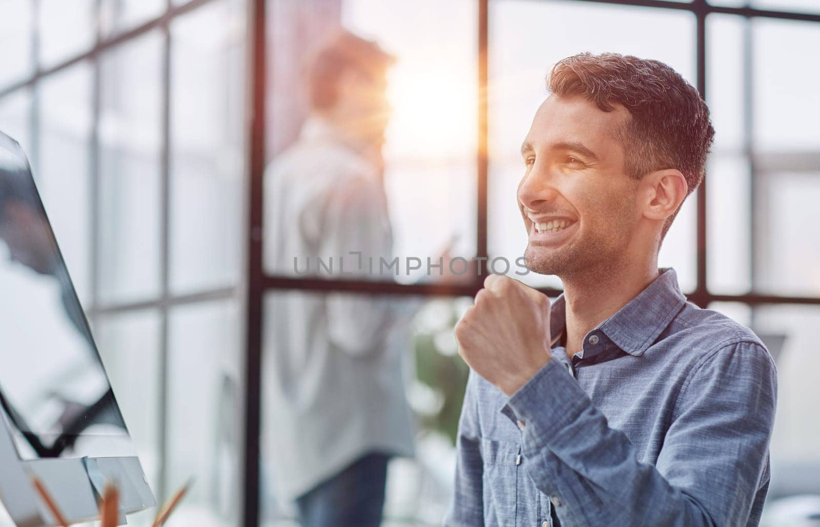 Excited modern businessman sitting at office desk and rejoicing his success