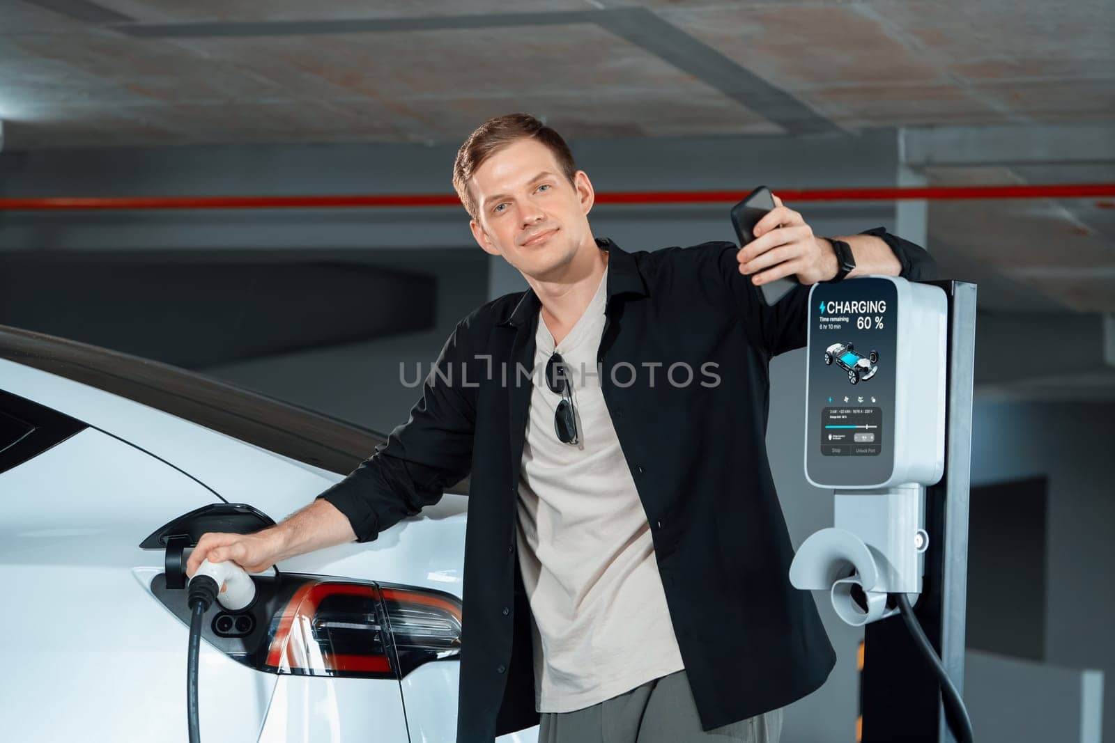 Young man travel with EV electric car to shopping center parking lot charging in downtown city showing urban sustainability lifestyle by green clean rechargeable energy of electric vehicle innards