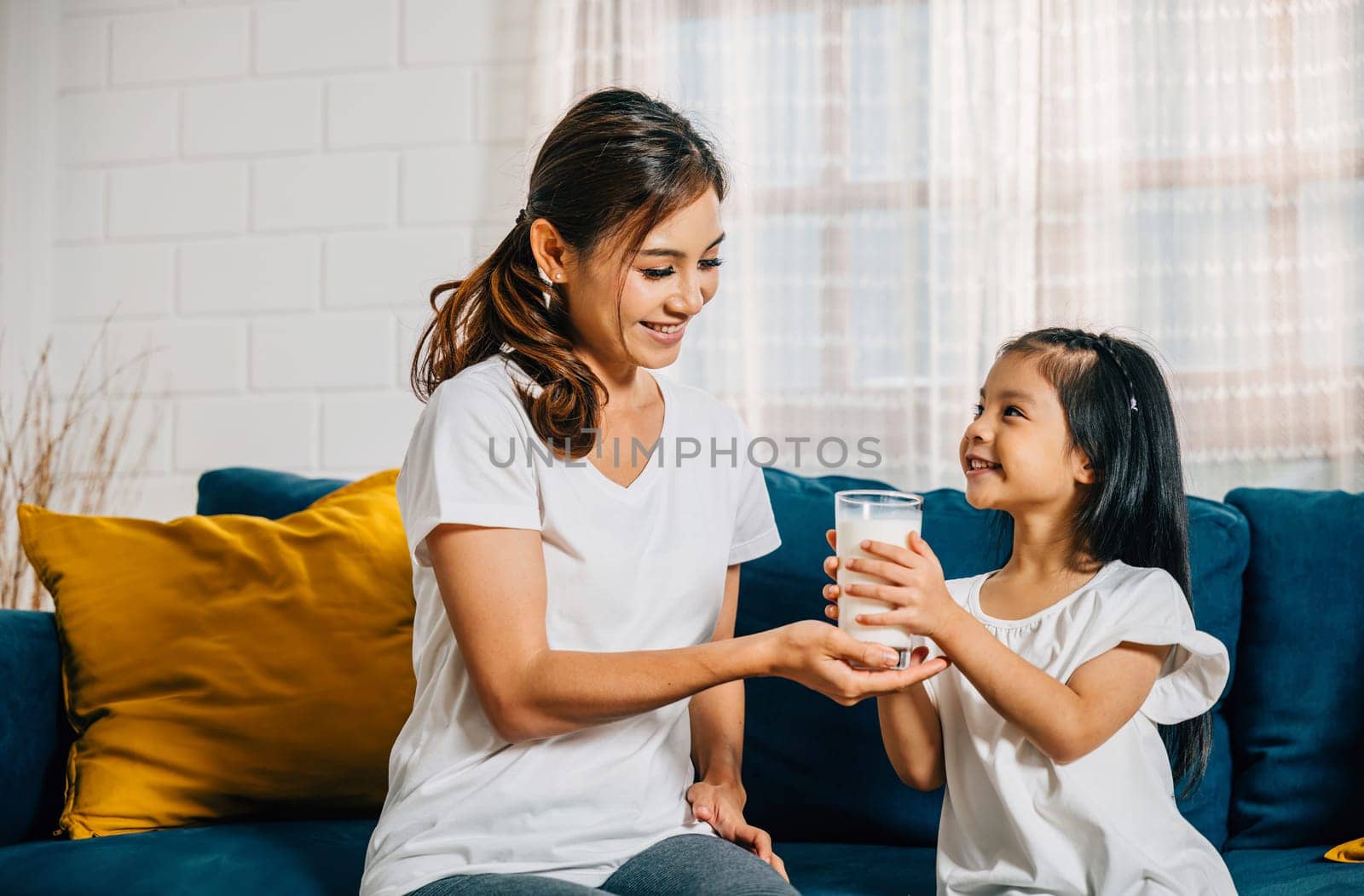A beautiful family morning as an Asian mother gives her daughter a glass of milk by Sorapop