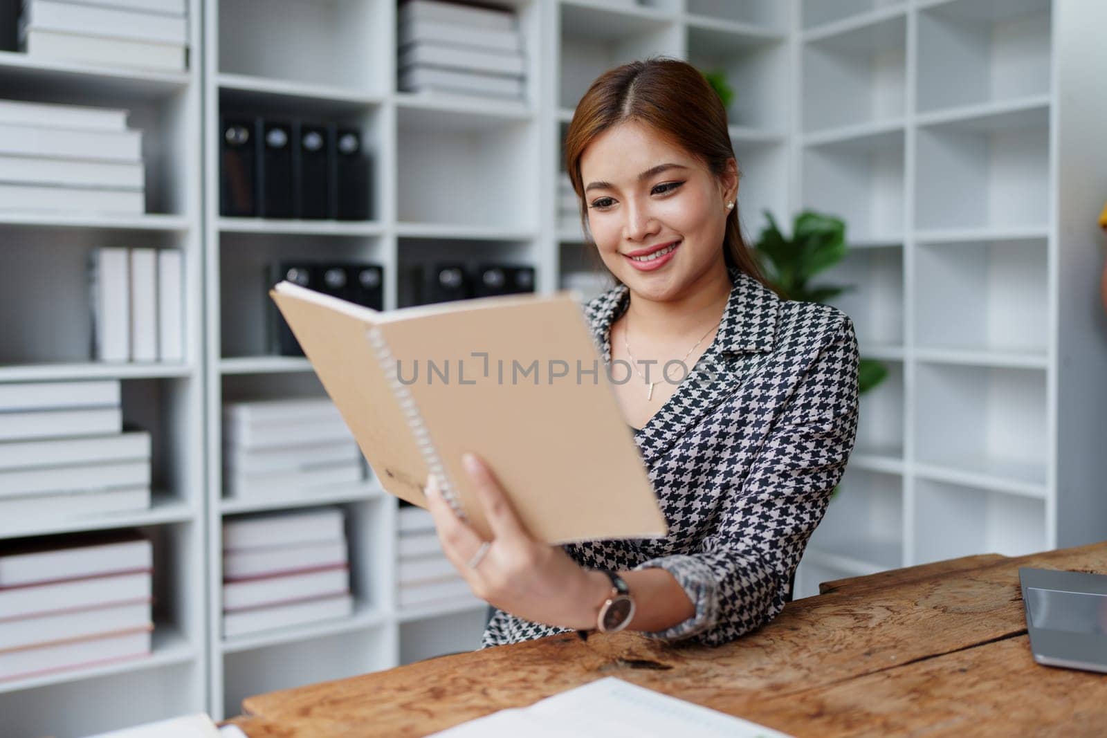 Portrait of a young Asian Woman showing a smiling face as she uses his notebook, computer and financial documents on her desk in the early morning hours by Manastrong