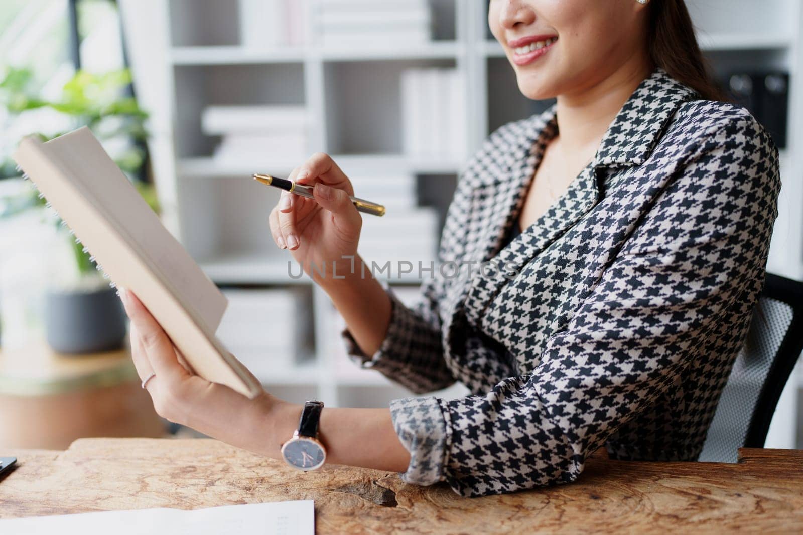 Portrait of a young Asian Woman showing a smiling face as she uses his notebook, computer and financial documents on her desk in the early morning hours.
