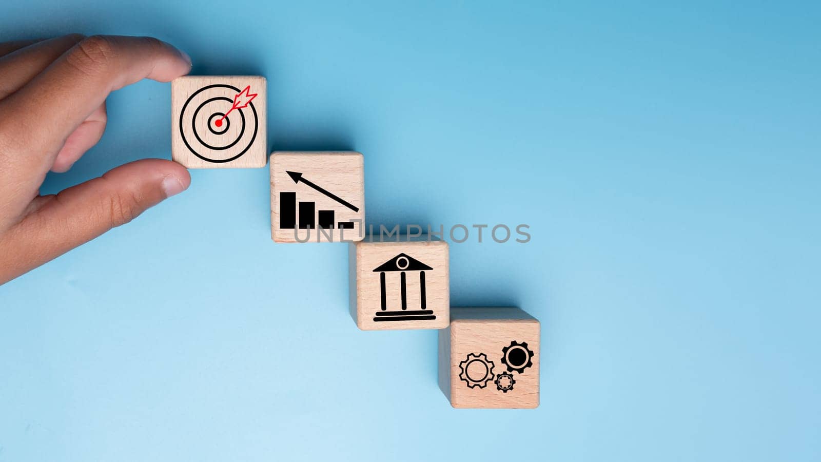 Human hands hold wooden blocks with target icons and business symbols on blue background, business goals and objectives concept, business competition. by Unimages2527