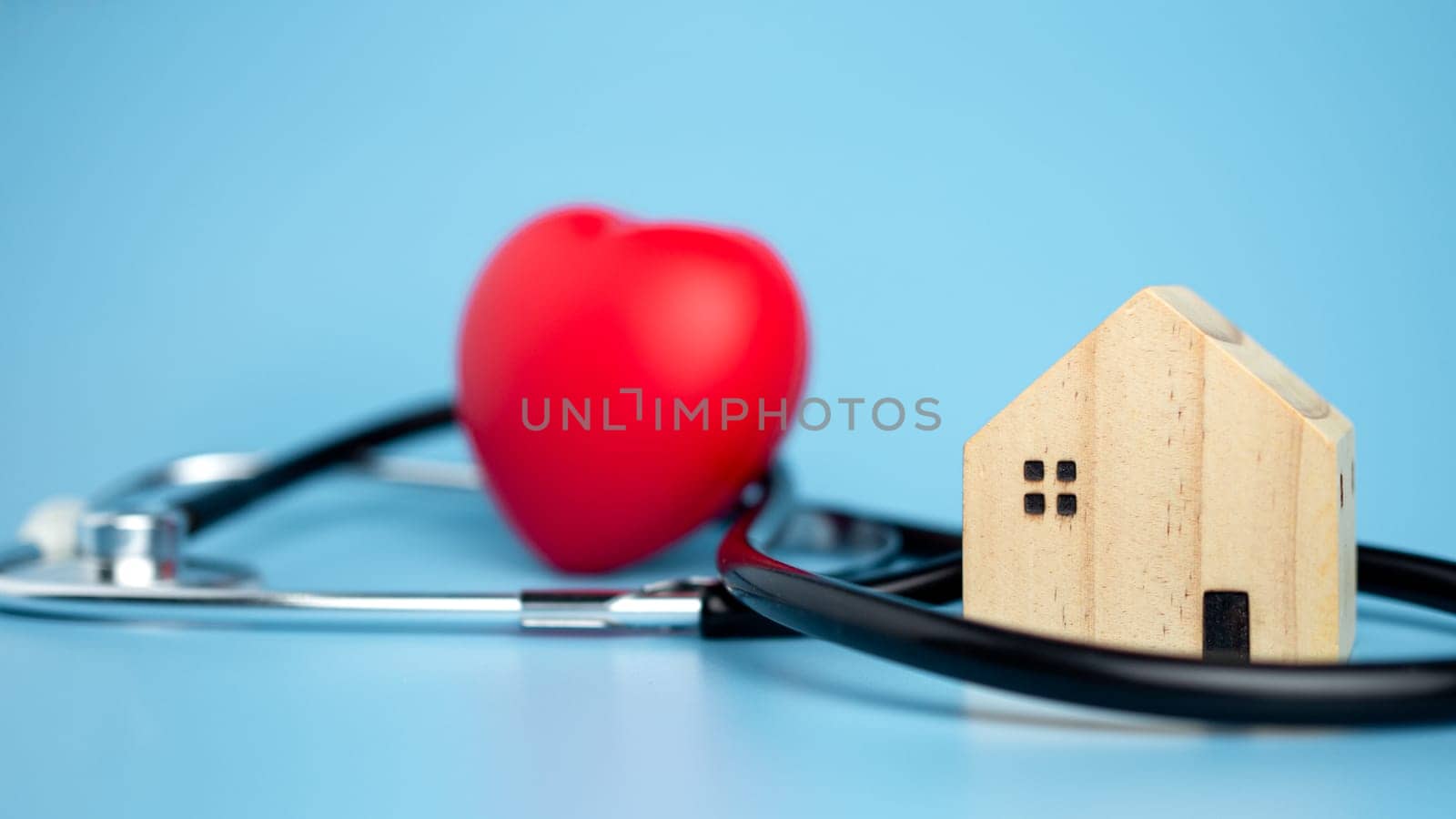 Concept of health insurance and medical welfare, small wooden house and red heart with stethoscope on blue background, health insurance and access to healthcare.