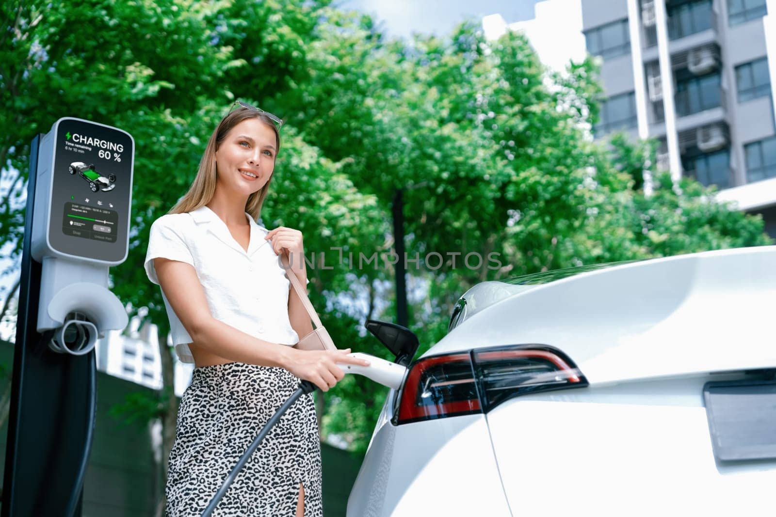Young woman travel with EV electric car charging in green sustainable city outdoor garden in summer. Urban sustainability lifestyle by green clean rechargeable energy of electric BEV vehicle innards
