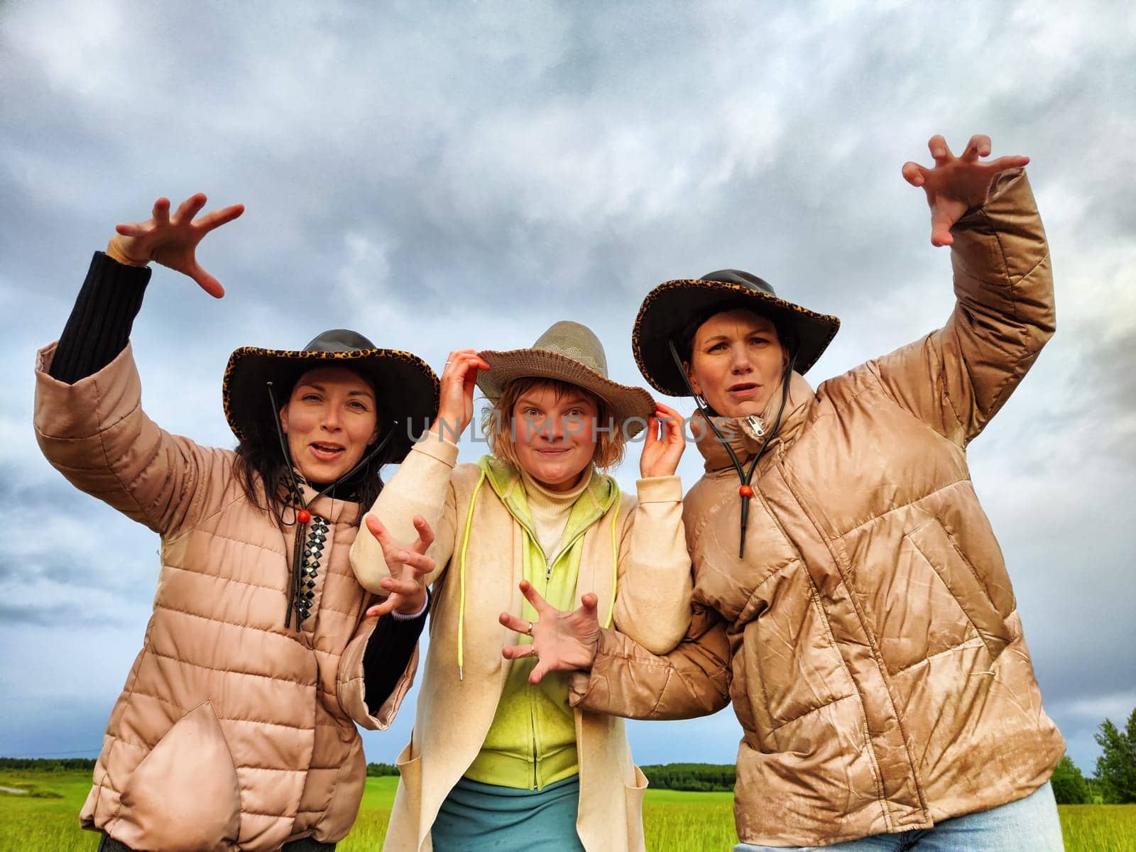 Adult girls looking like a cowboys in hats in a field and with a stormy sky with clouds posing in the rain. Women having fun outdoors on rural and rustic nature