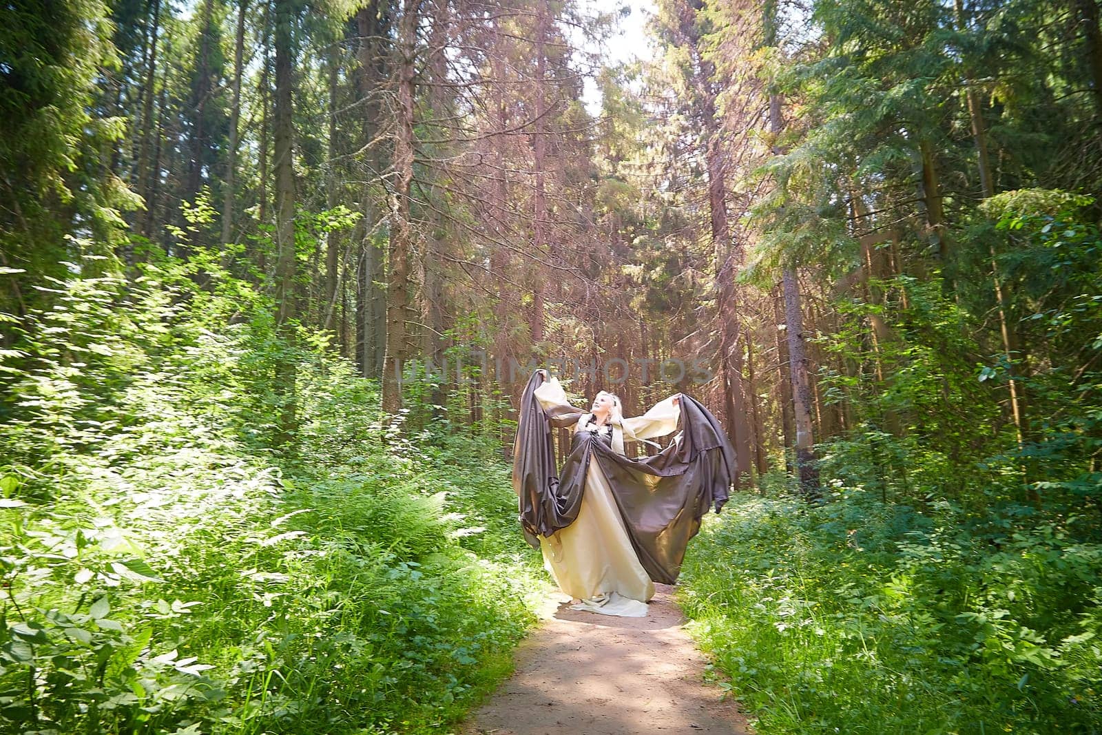 Adult mature woman 40-60 in a green long fairy dress in forest. Photo shoot in style of dryad and queen of nature. Fairy in beautiful green summer forest. Concept of caring for nature