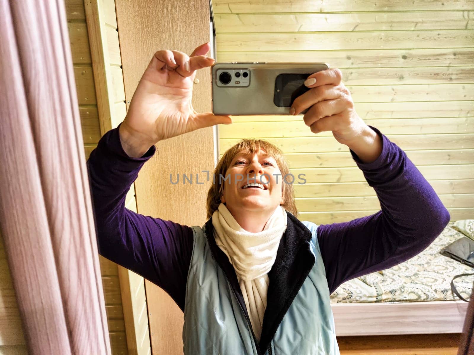 Middle-aged woman using smartphone for selfie and blogging. Female blogger poses in a photo. The girl admires herself in the mirror