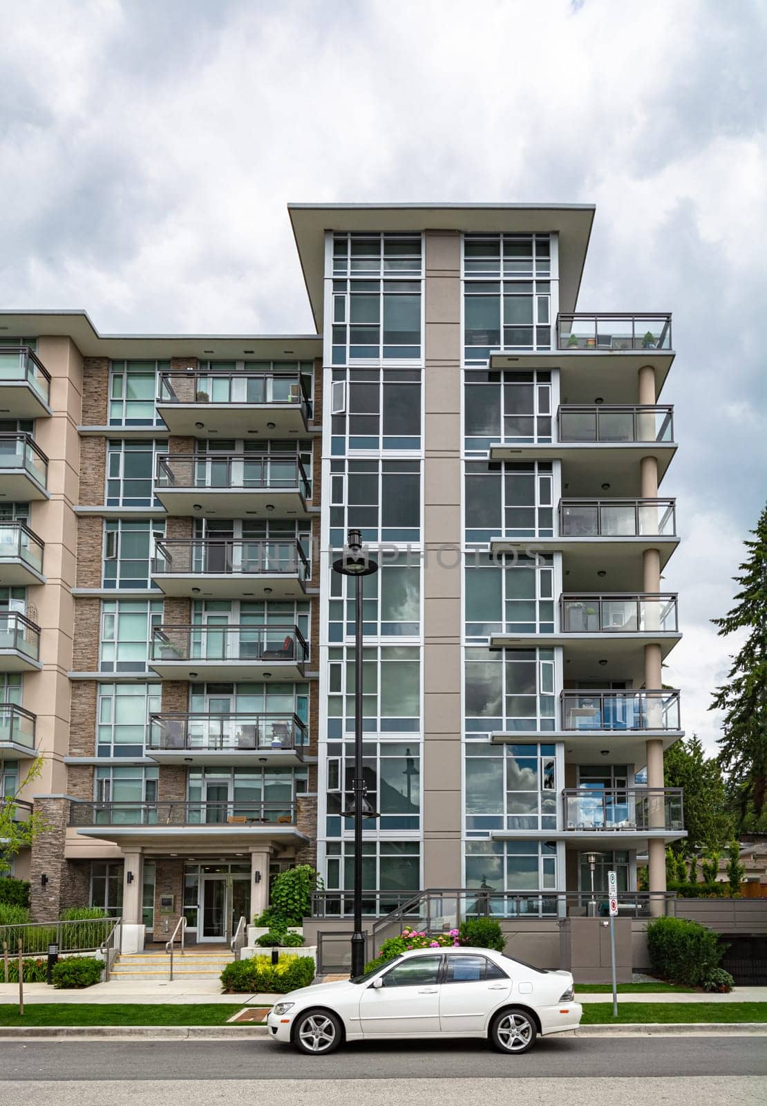 New residential low-rise building with cars parked on the street in front on cloudy sky background