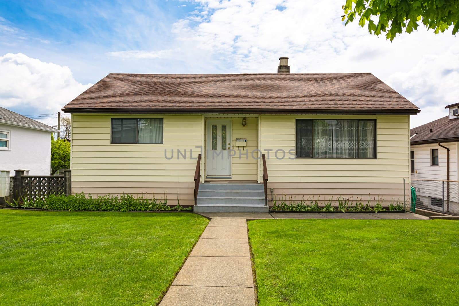 Modest family house with green lawn in front. Old residential house on cloudy day in Canada