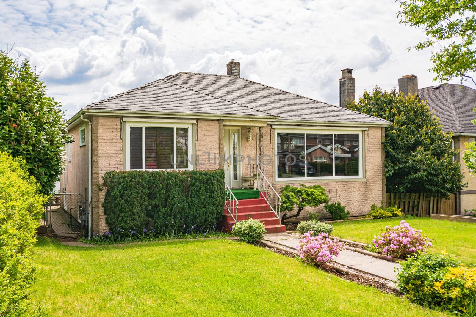 Modest family house with green lawn in front and stone wall texture. Old residential house on cloudy day in Canada