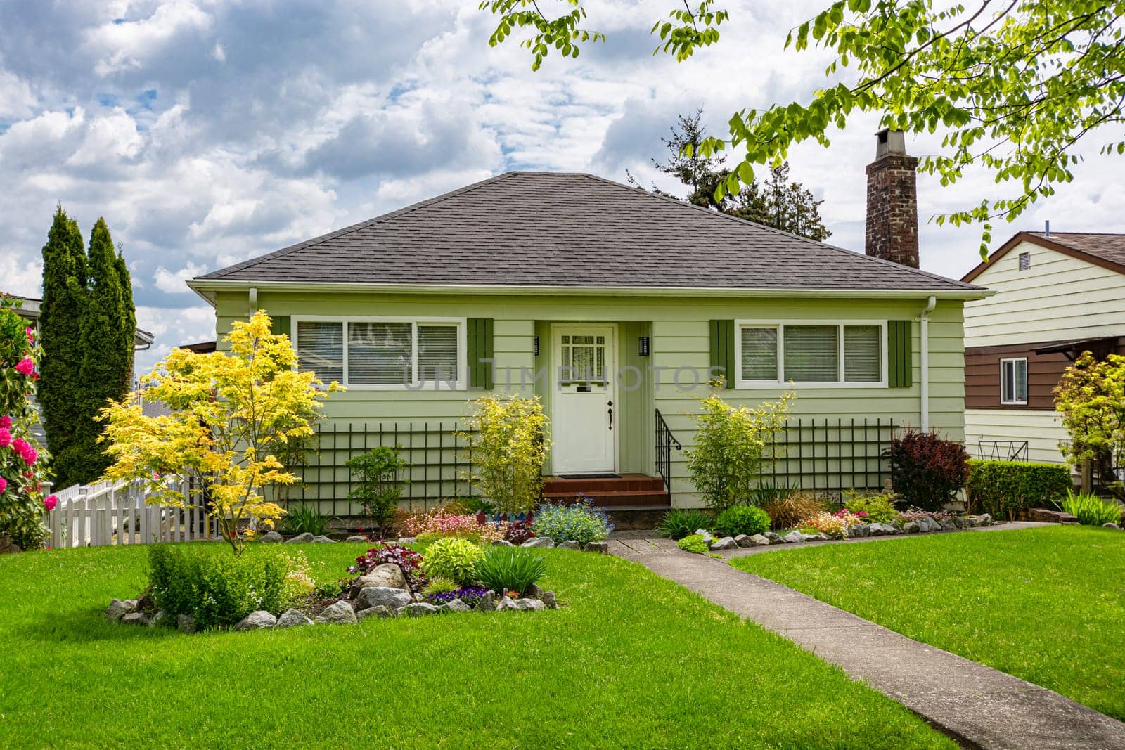 Perfect neighbourhood. Neat and nice average family house with green lawn in front. Old residential house on cloudy sky background