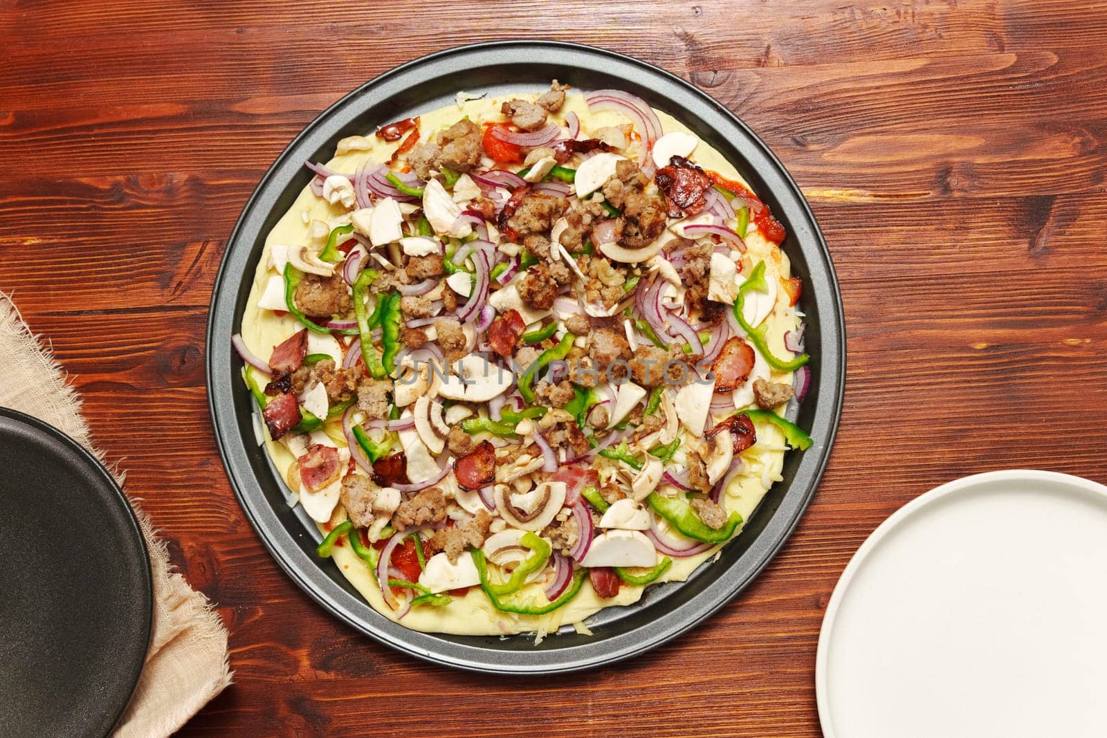 Raw St. Louis-Style Pizza homemade on a wooden background, with cheese, pepper, bacon onion