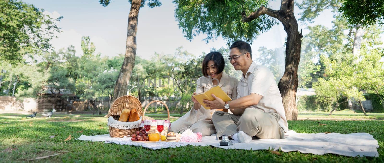 Cheerful elderly couple asian wear casual clothes sitting in the park having a party together by nateemee