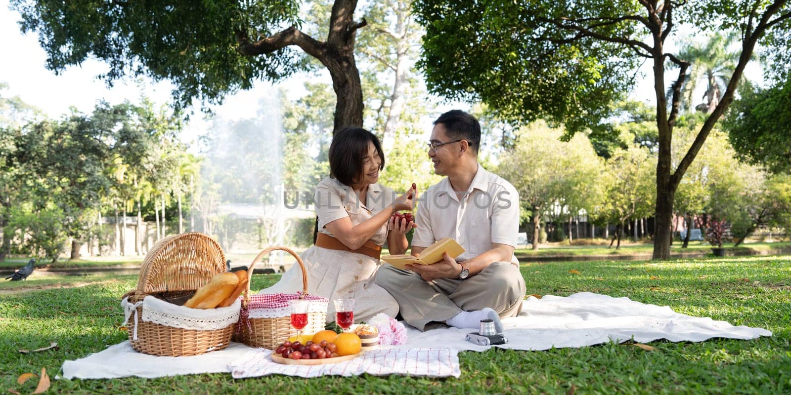 Cheerful elderly couple asian wear casual clothes sitting in the park having a party together by nateemee