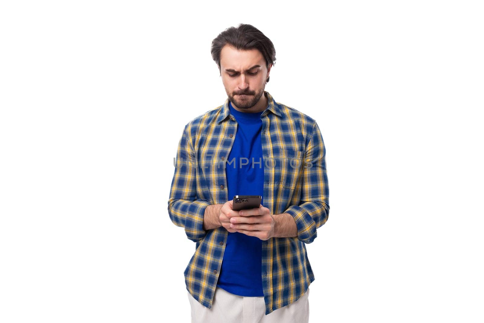 young caucasian brunette with a beard is dressed in a blue plaid shirt and t-shirt watching a video on the phone on a white background.