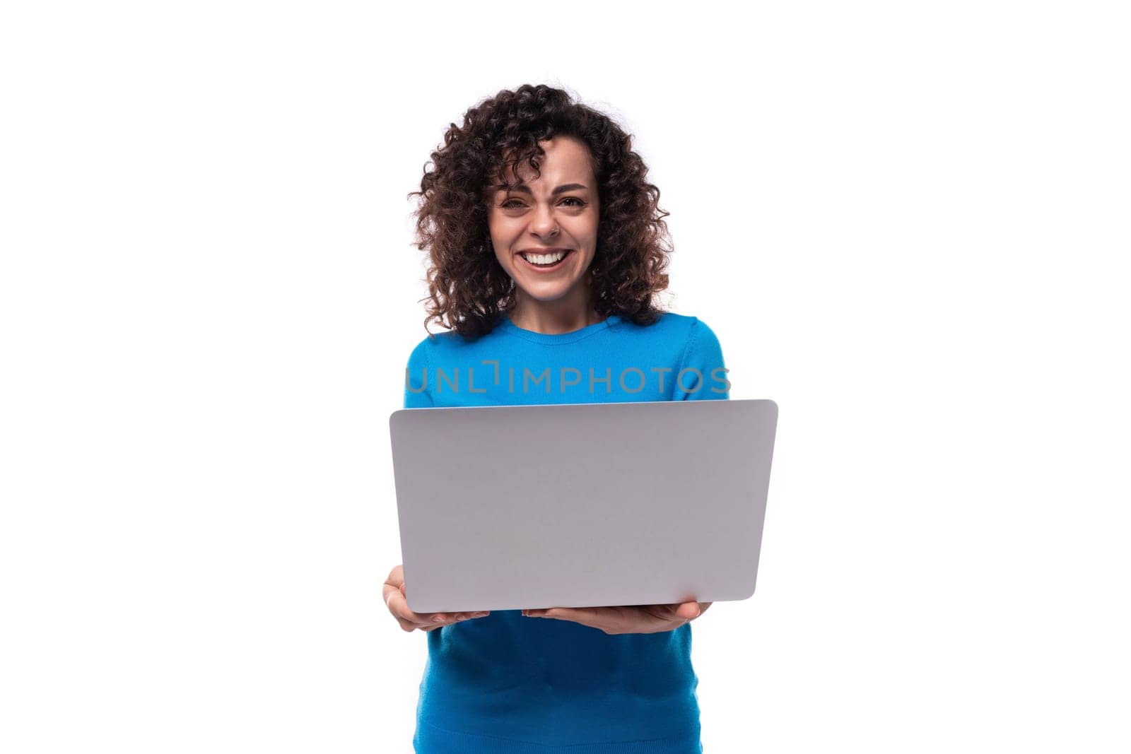 young curly woman with black hair is wearing a blue corporate t-shirt and holding a laptop.