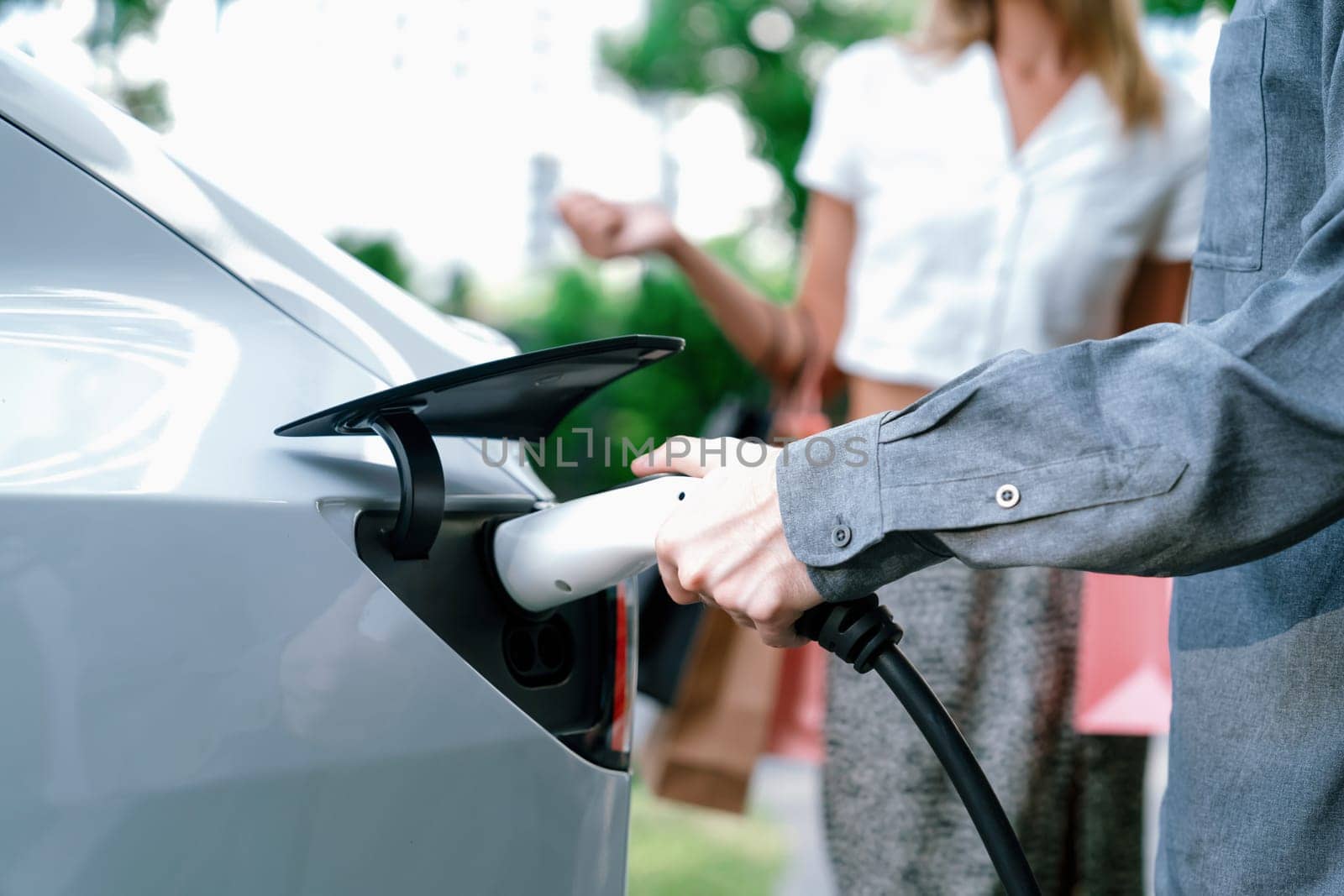 Young couple travel with EV electric car in green sustainable city innards by biancoblue