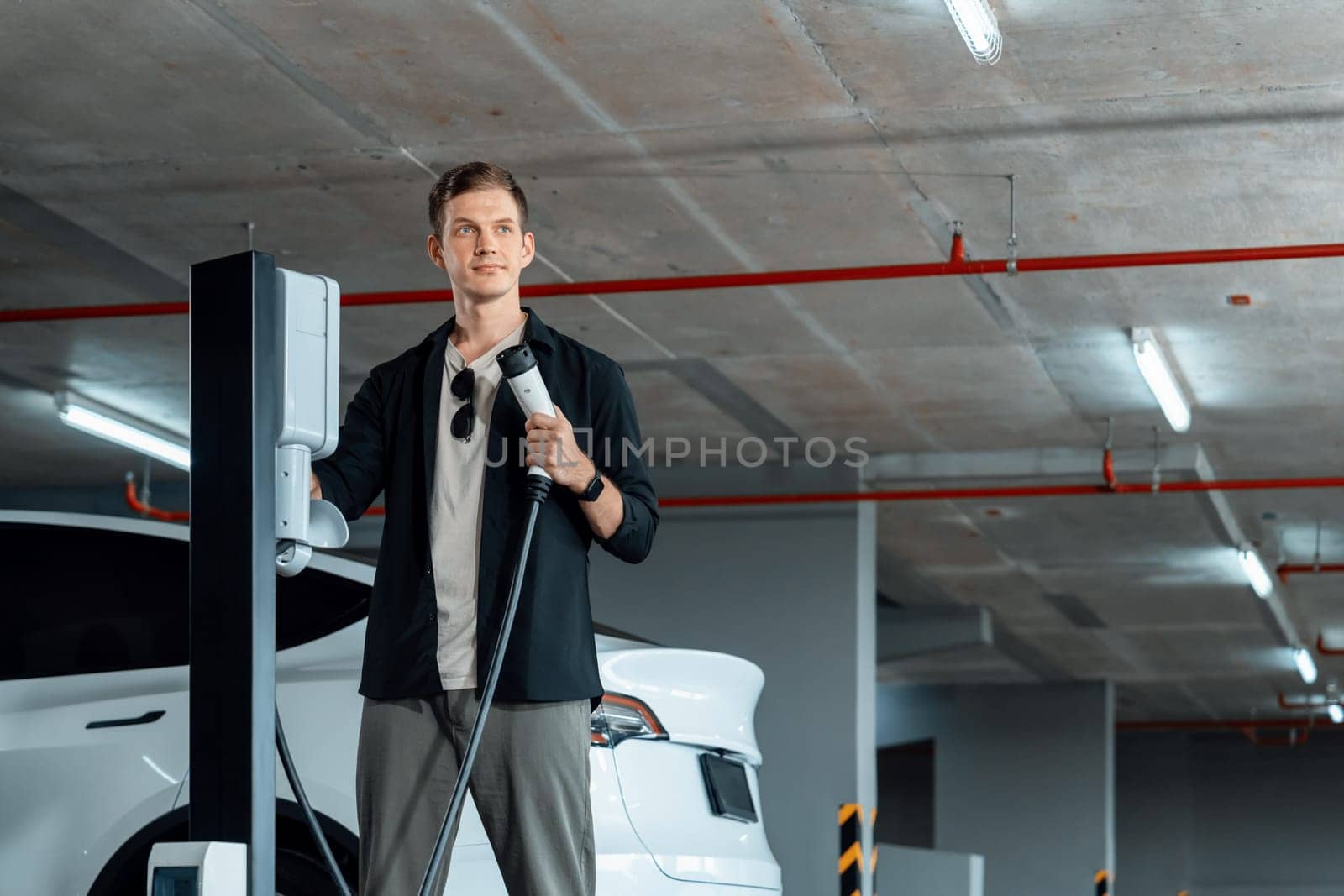 Young man travel with EV electric car to shopping center parking lot charging in downtown city showing urban sustainability lifestyle by green clean rechargeable energy of electric vehicle innards