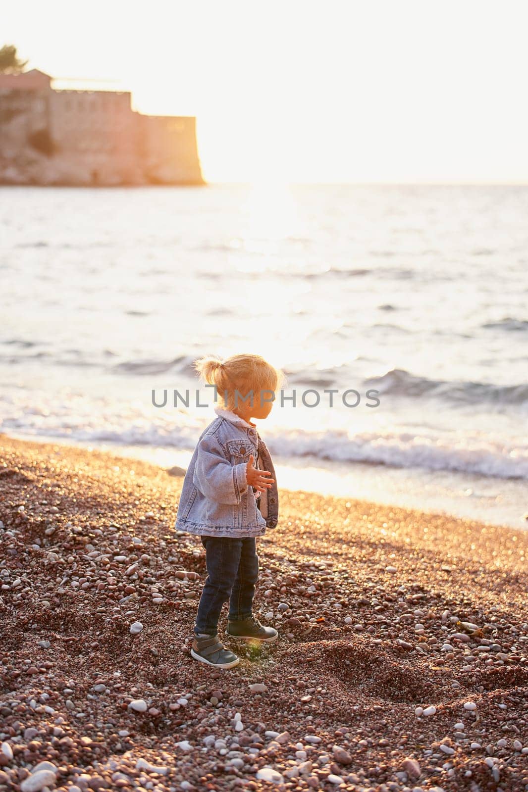 Little girl stands on a pebble beach and looks at the sea. High quality photo