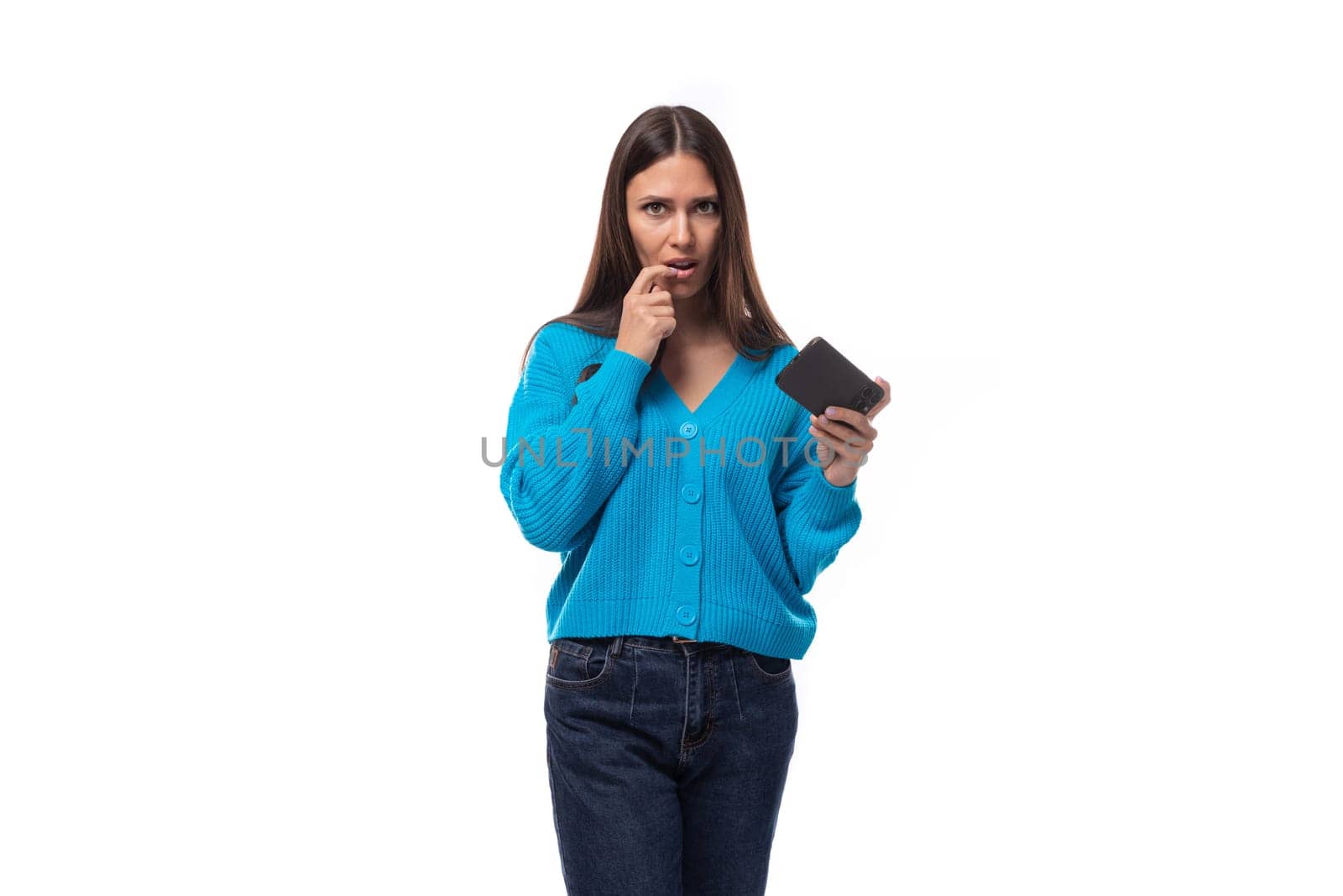 stylish young brunette lady dressed in a blue casual buttoned cardigan looks attentively at the phone.