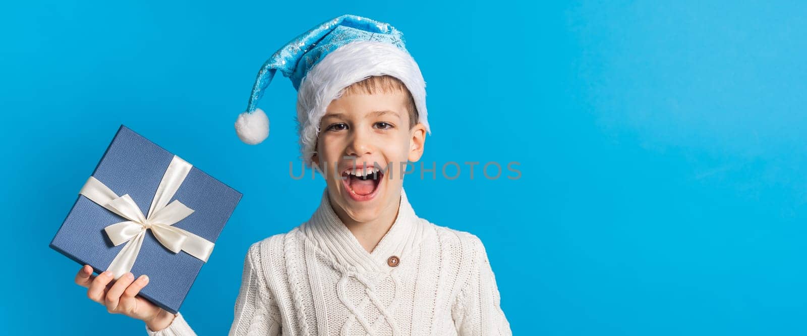 Child boy gift. Kid close-up holds gift box. Shopping time. Banner header with copy space on blue background. by Satura86