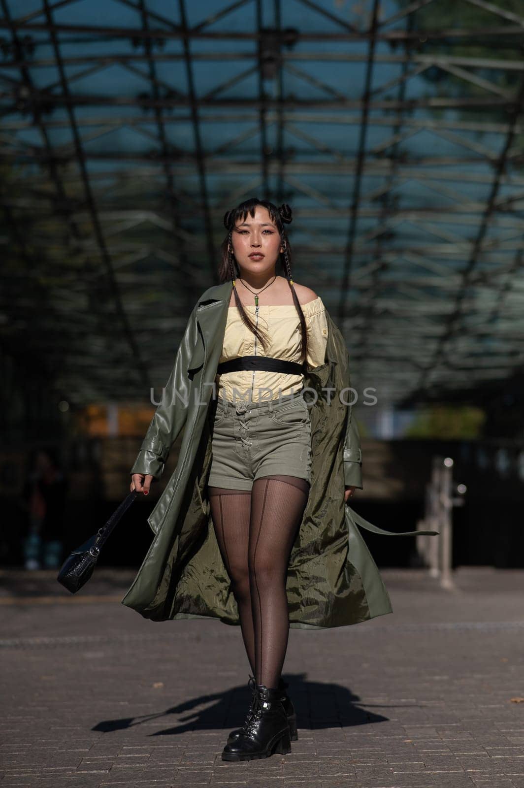 A beautiful Asian woman in shorts and a green leather coat comes out of the subway