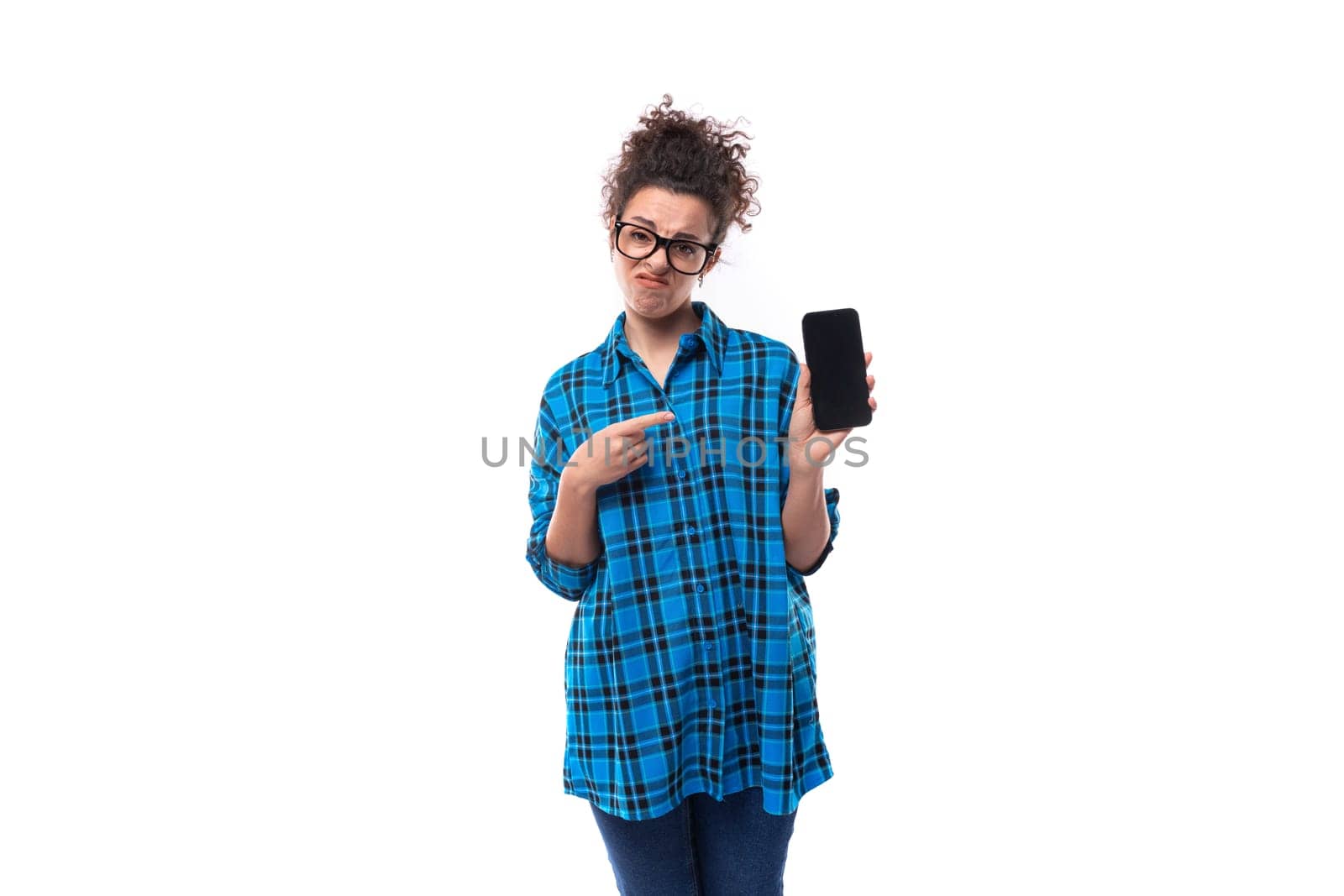 cute young pretty woman with curled hair in a blue shirt shows the screen of a smartphone with a mockup by TRMK