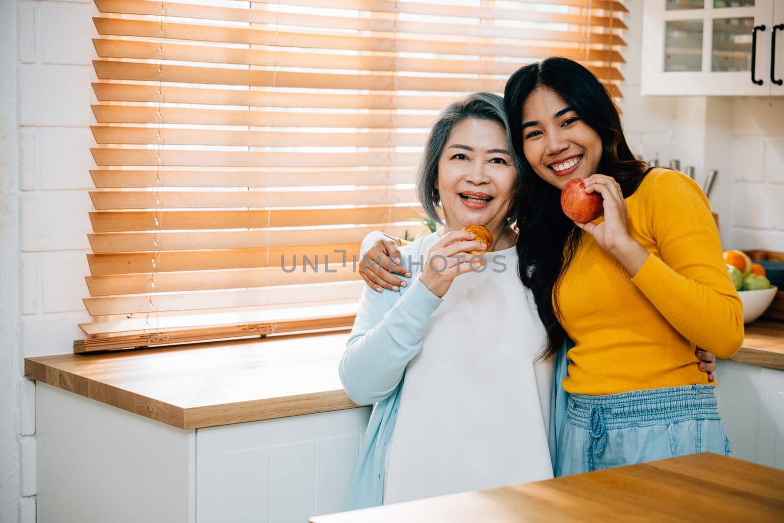 Kitchen scene at home features an elderly mother and her daughter, young Asian woman. moment of togetherness while daughter teaches and assists her mother. beautiful portrait of family bonding. by Sorapop