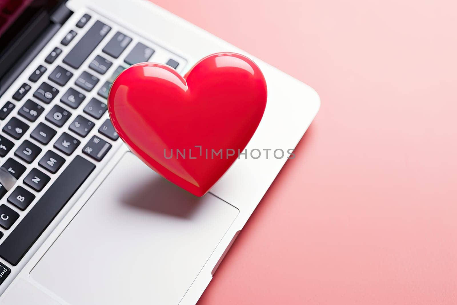 Close up laptop keyboard with a red heart over a pink table with copy space. Online dating concept by papatonic