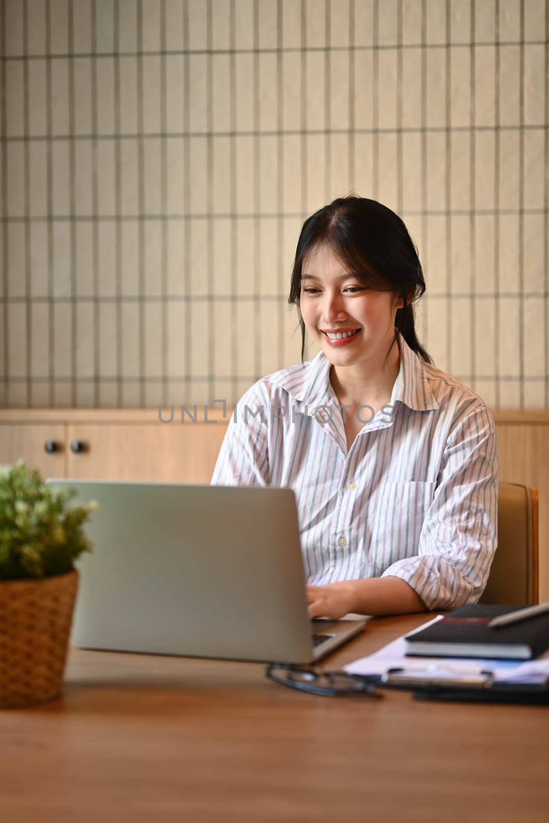 Attractive young female employee working with laptop at modern workplace.