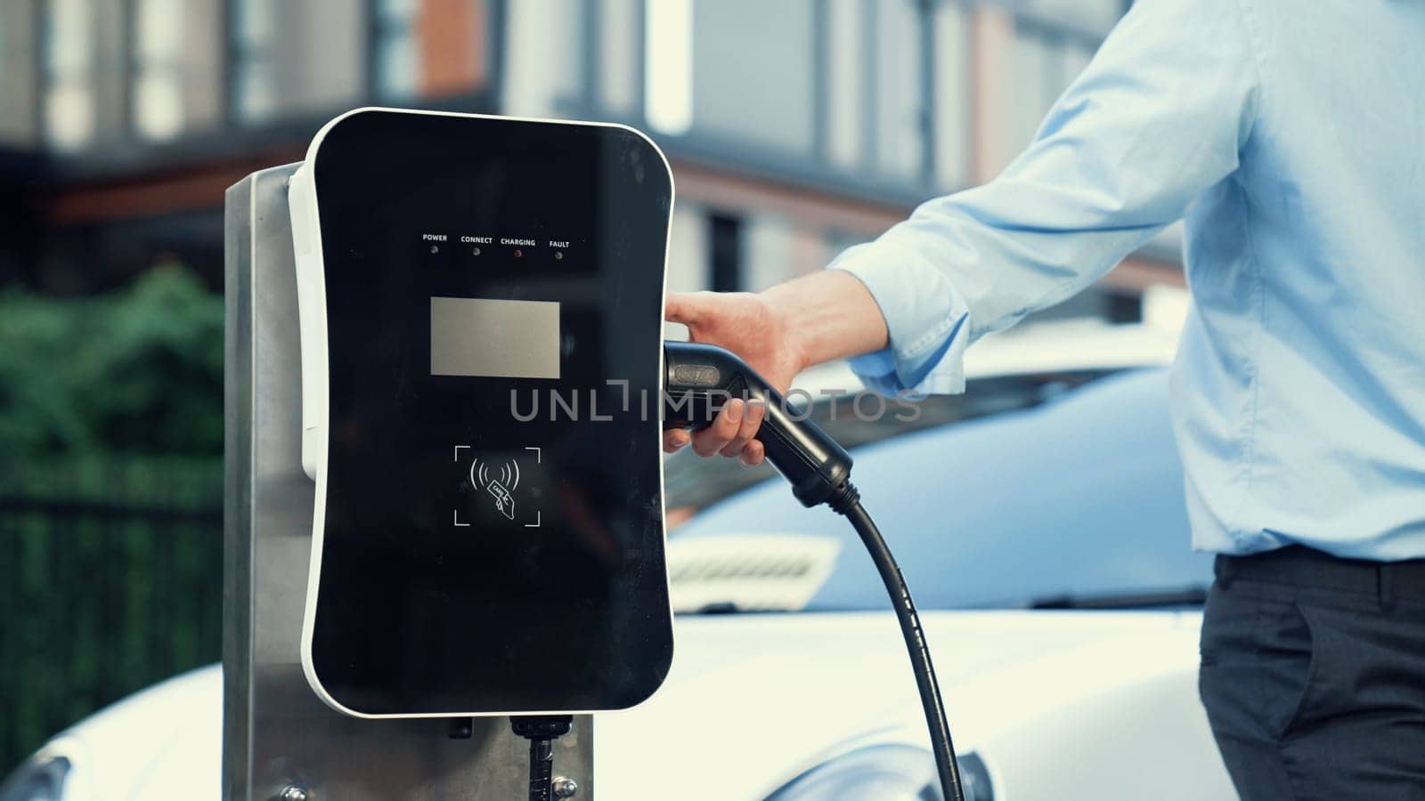 Progressive businessman plugs charger plug from charging station to his EV. by biancoblue