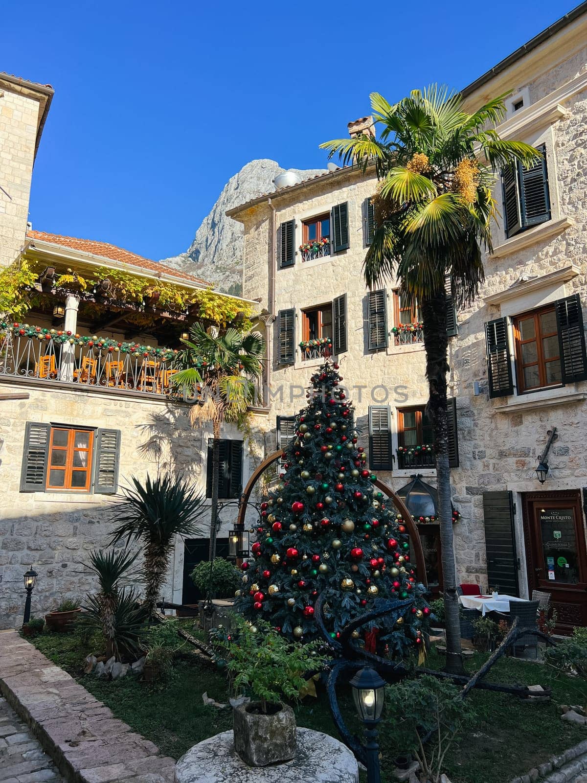 Decorated Christmas tree in the courtyard of an old stone house among palm trees. High quality photo