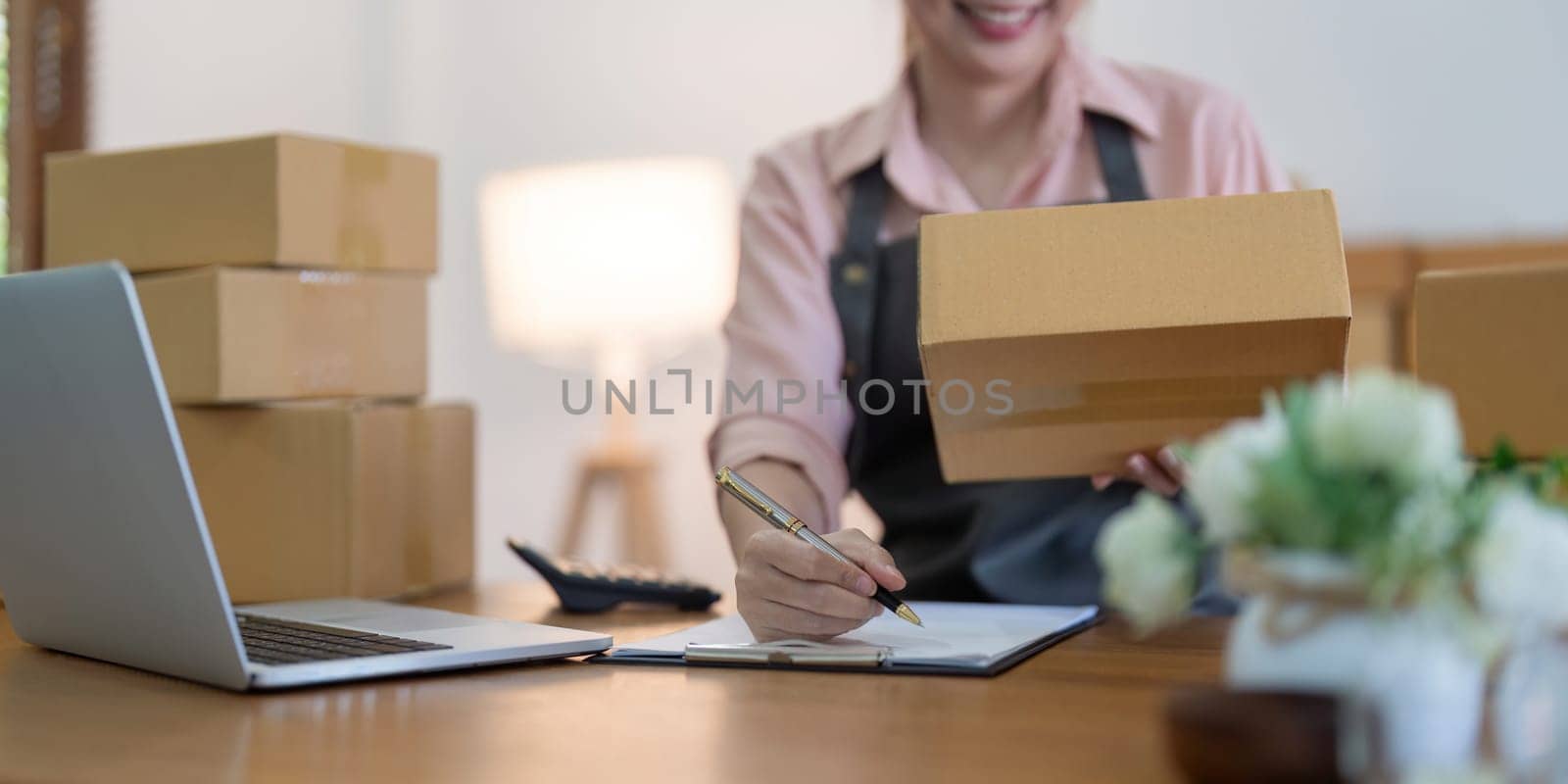 Asian woman entrepreneur prepare parcel box and check online order on laptop computer for commercial checking delivery. online marketing, packing box, SME seller. startup business concept.