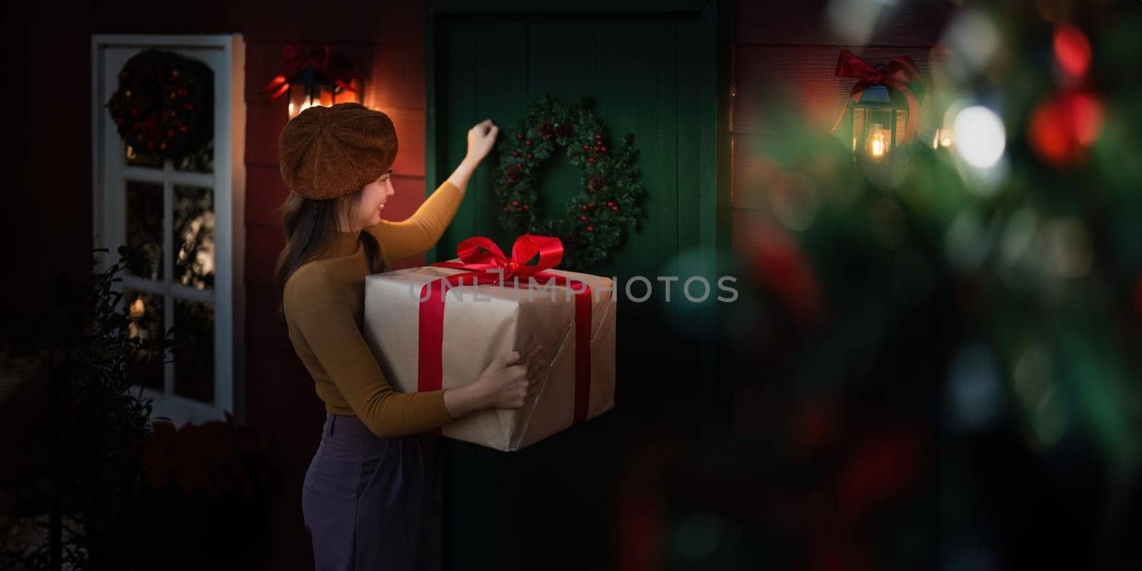 Happy woman wearing Santa hat holding of gift box. Positive emotional Santa girl. with a beautifully decorated Christmas tree serving as the background. festive Xmas concept.