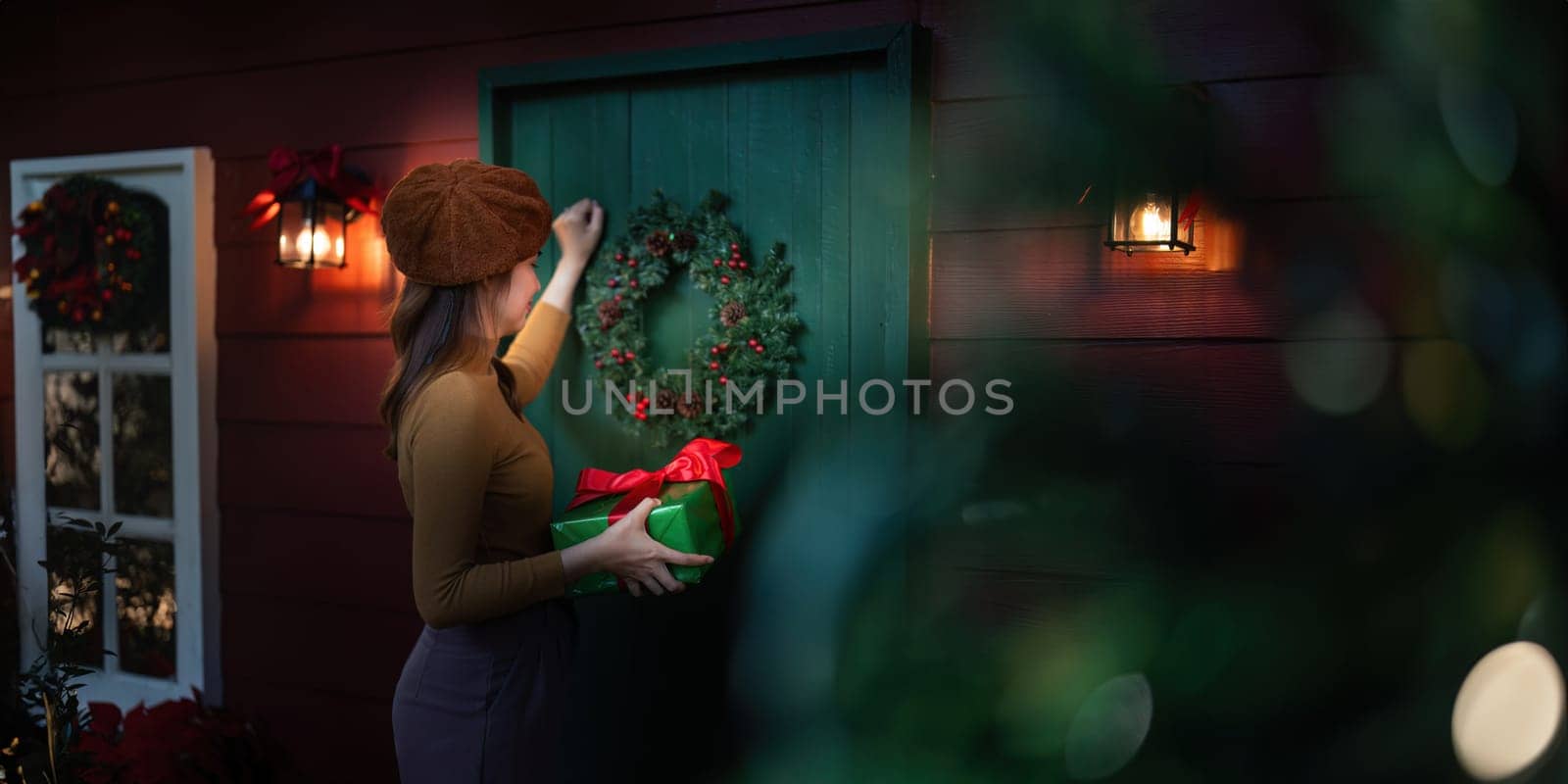 Happy woman wearing Santa hat holding of gift box. Positive emotional Santa girl. with a beautifully decorated Christmas tree serving as the background. festive Xmas concept by nateemee