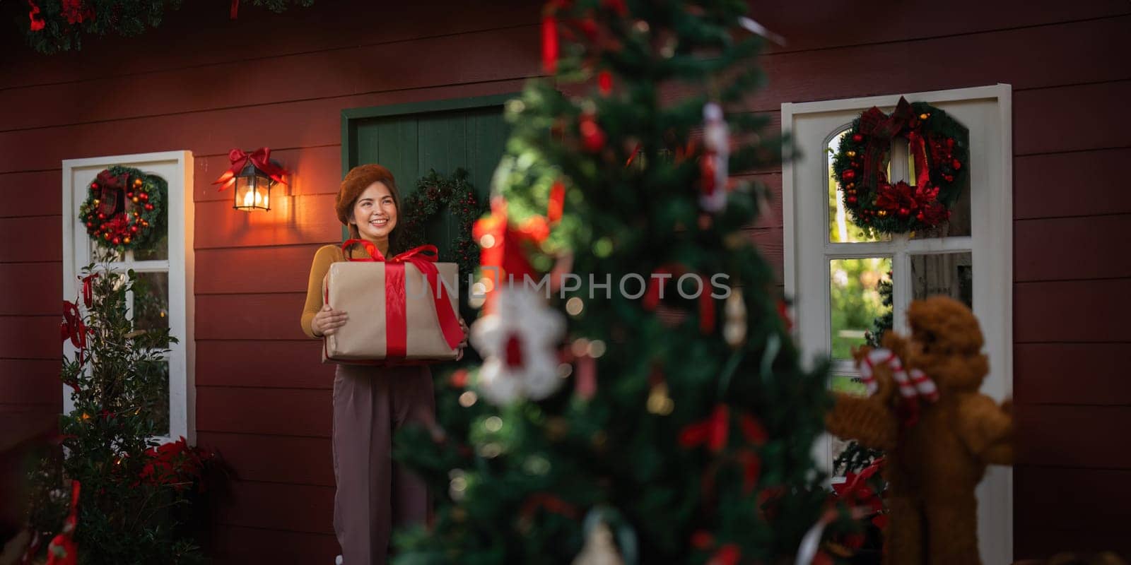 Happy woman wearing Santa hat holding of gift box. Positive emotional Santa girl. with a beautifully decorated Christmas tree serving as the background. festive Xmas concept.