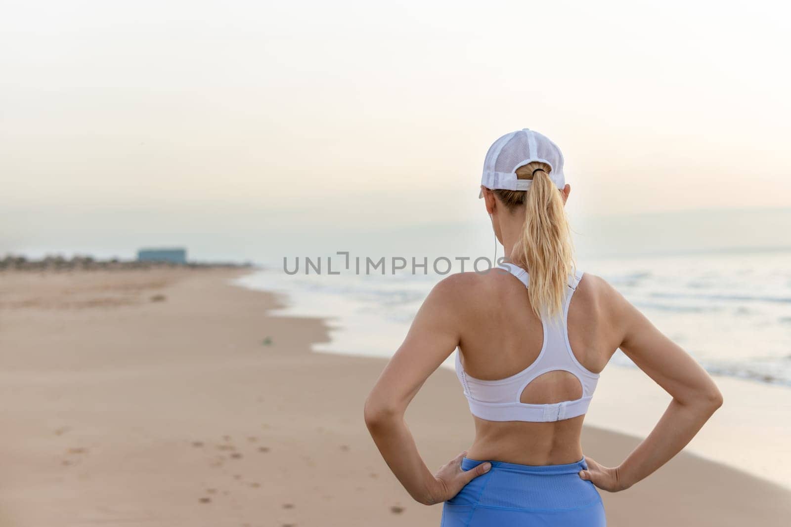 a thin girl in blue tights and a white top stands against the backdrop of the sea at dawn doing exercises, the concept of a healthy lifestyle. High quality photo