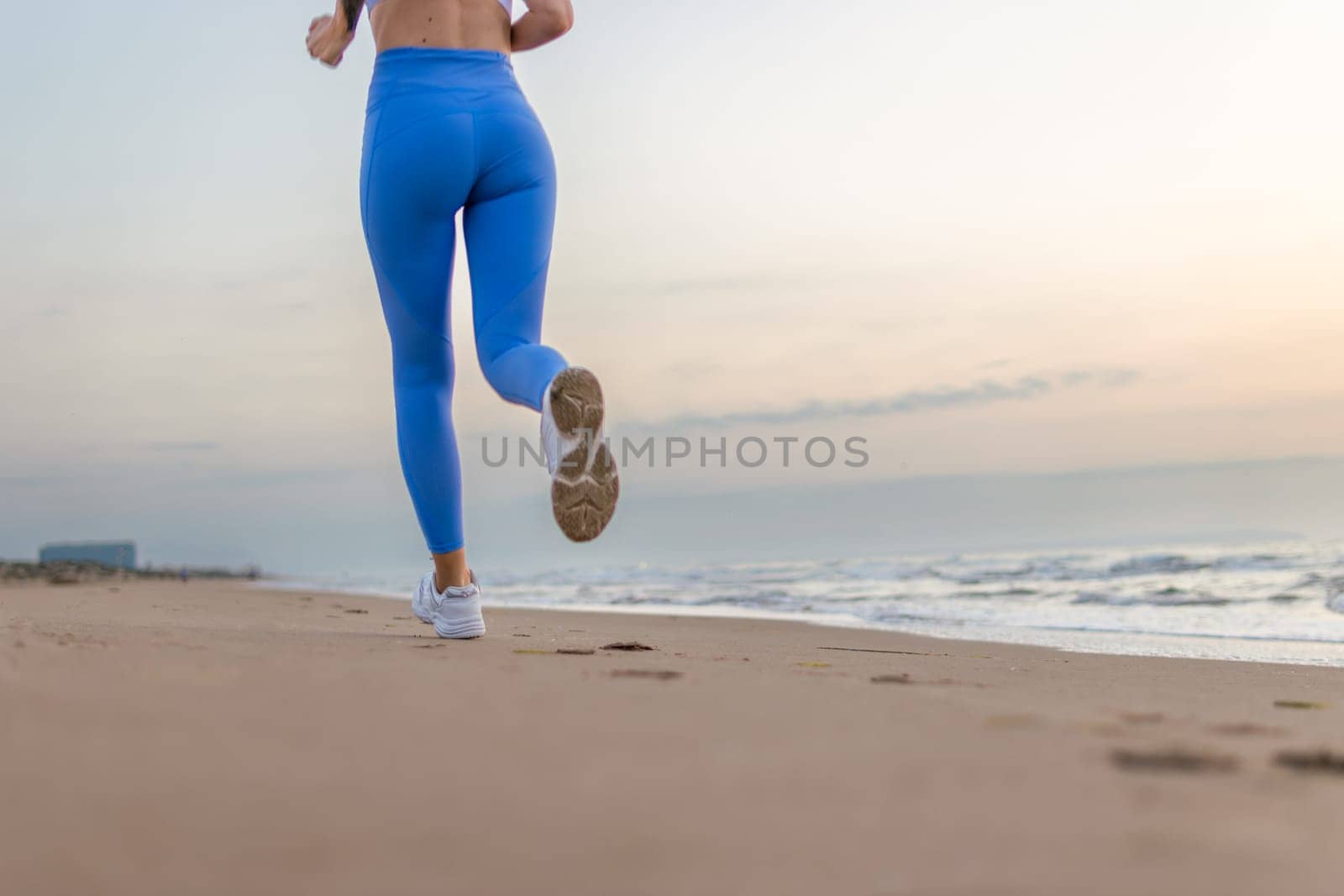 legs of a girl in blue leggings and sneakers running along the beach at dawn with space for inscription. High quality photo