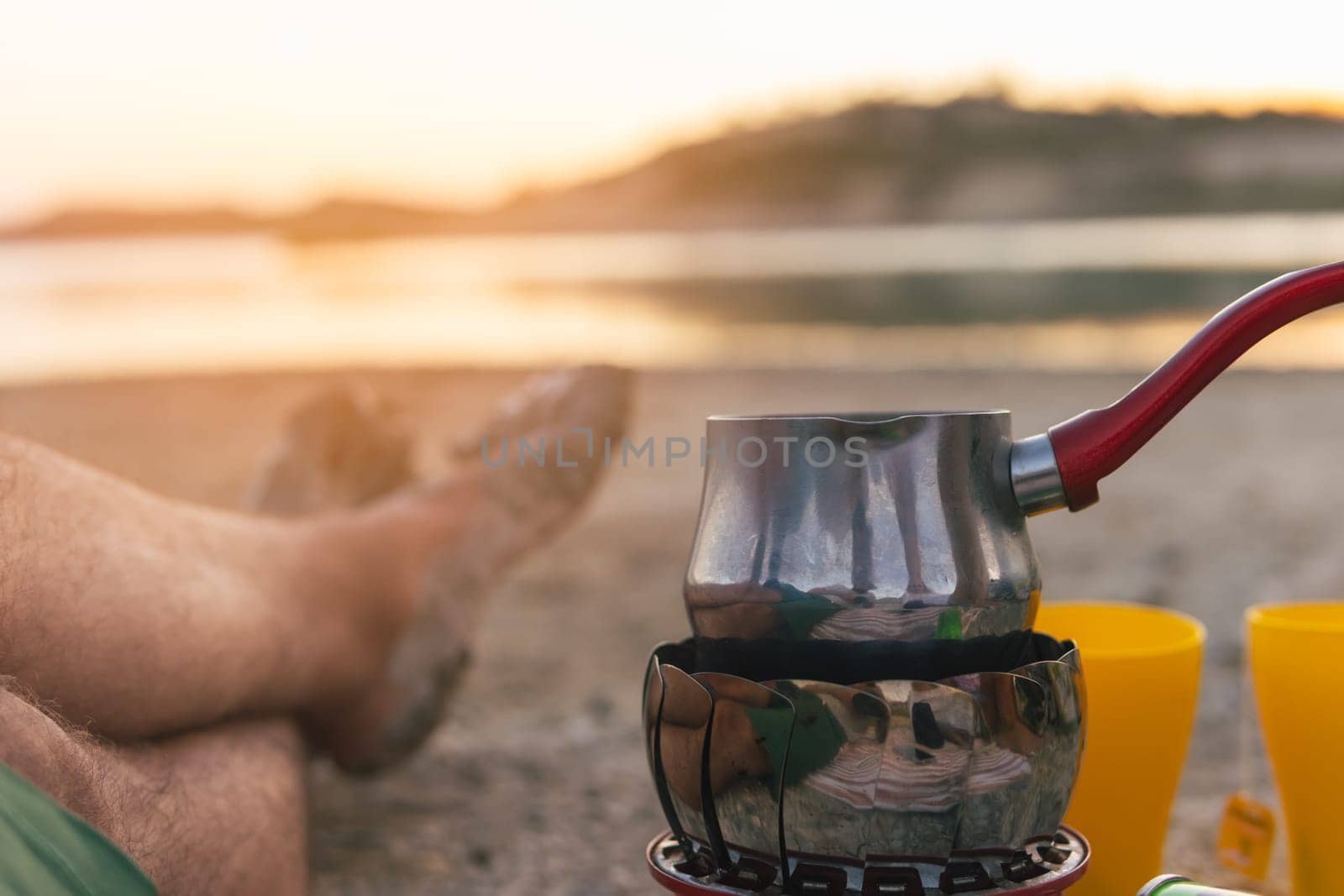 male legs against the backdrop of a lake close-up, next to there is a burner with a small pan for water. High quality photo