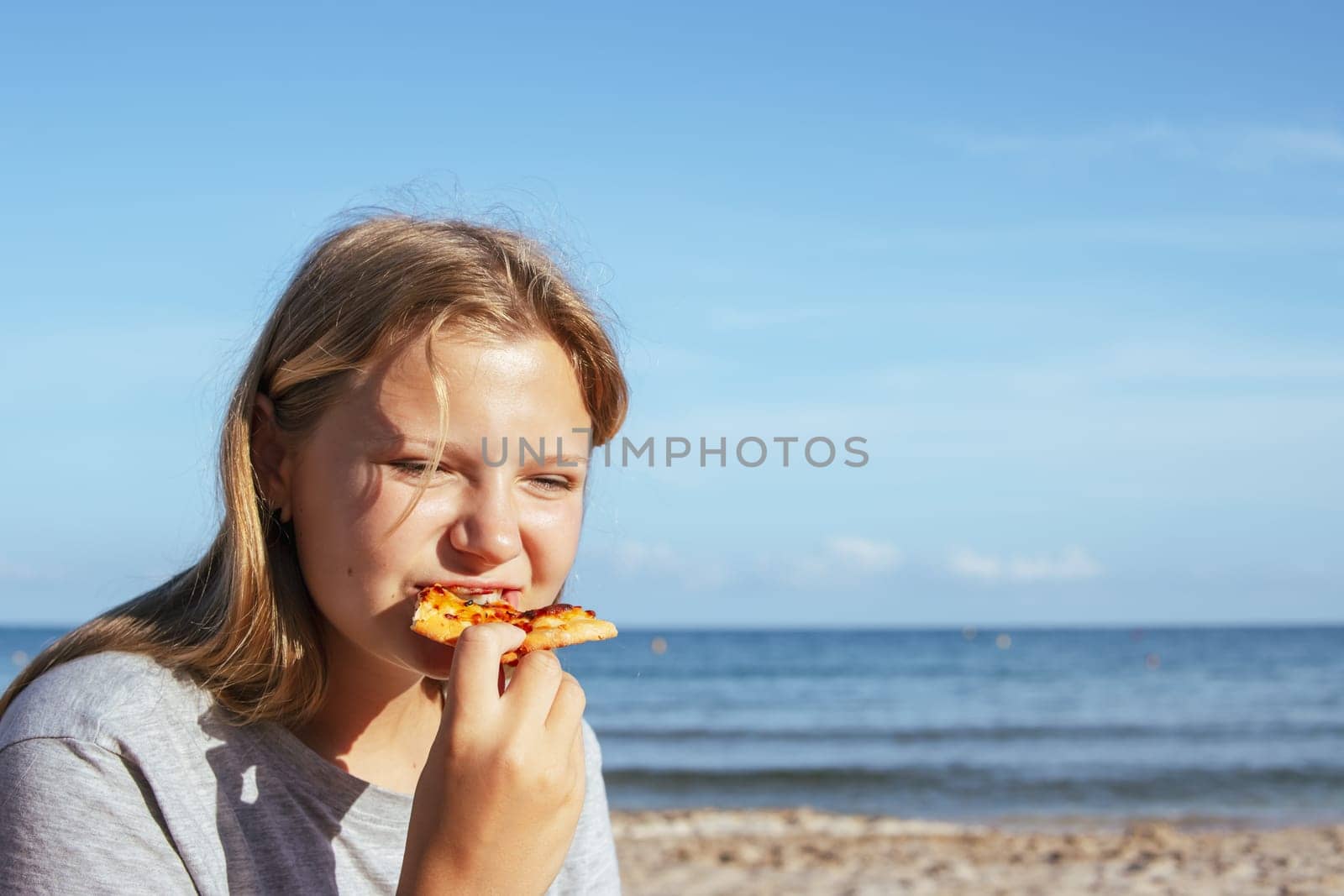 teenage girl of European appearance eats a slice of pizza on the seashore. High quality photo