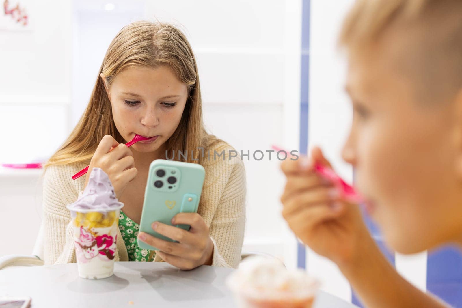 a boy and a girl eat ice cream in a summer cafe in a summer cafe, a girl looks at a photo on her phone, family vacation concept. High quality photo