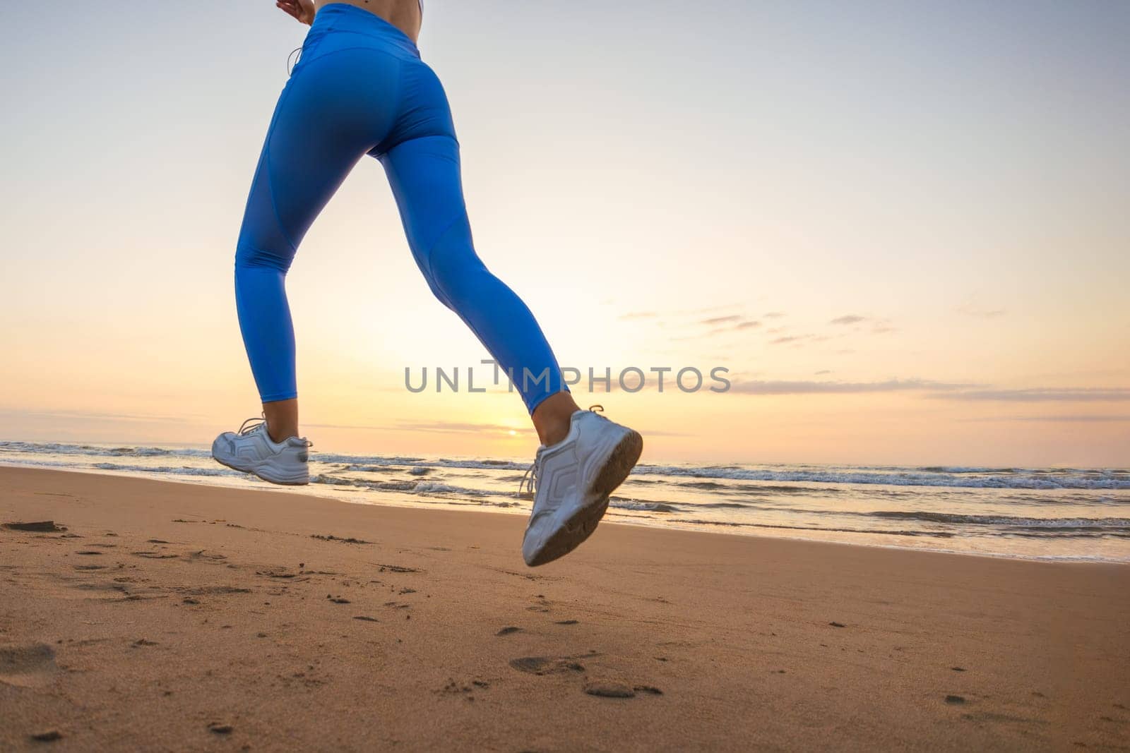 legs of a girl in leggings and sneakers running along the beach at dawn with space for inscription by PopOff