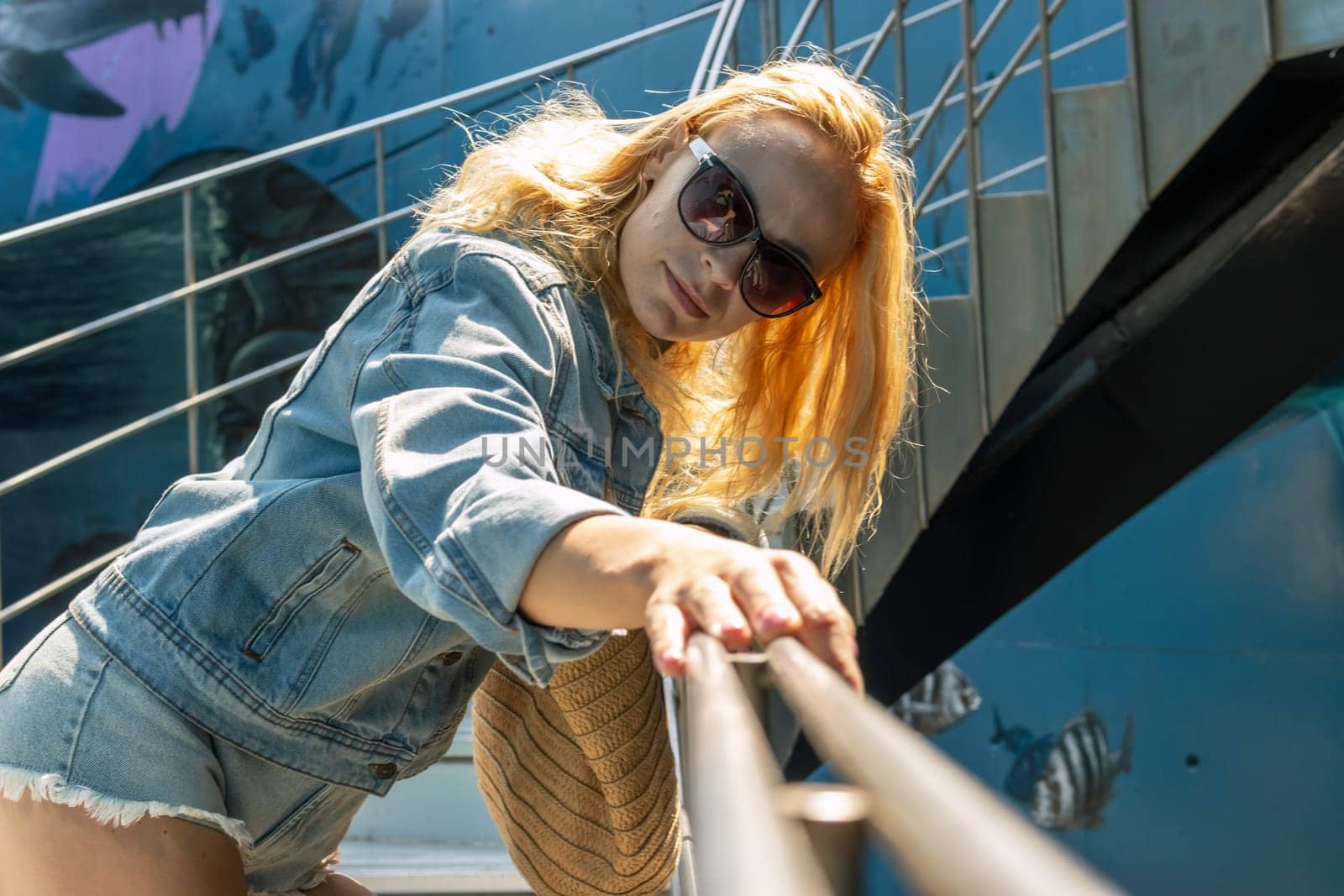 Outdoor portrait of a young beautiful fashionable girl posing on the street. Model in a stylish denim jacket and sunglasses. Women's fashion concept. Copy, empty space for text. High quality photo