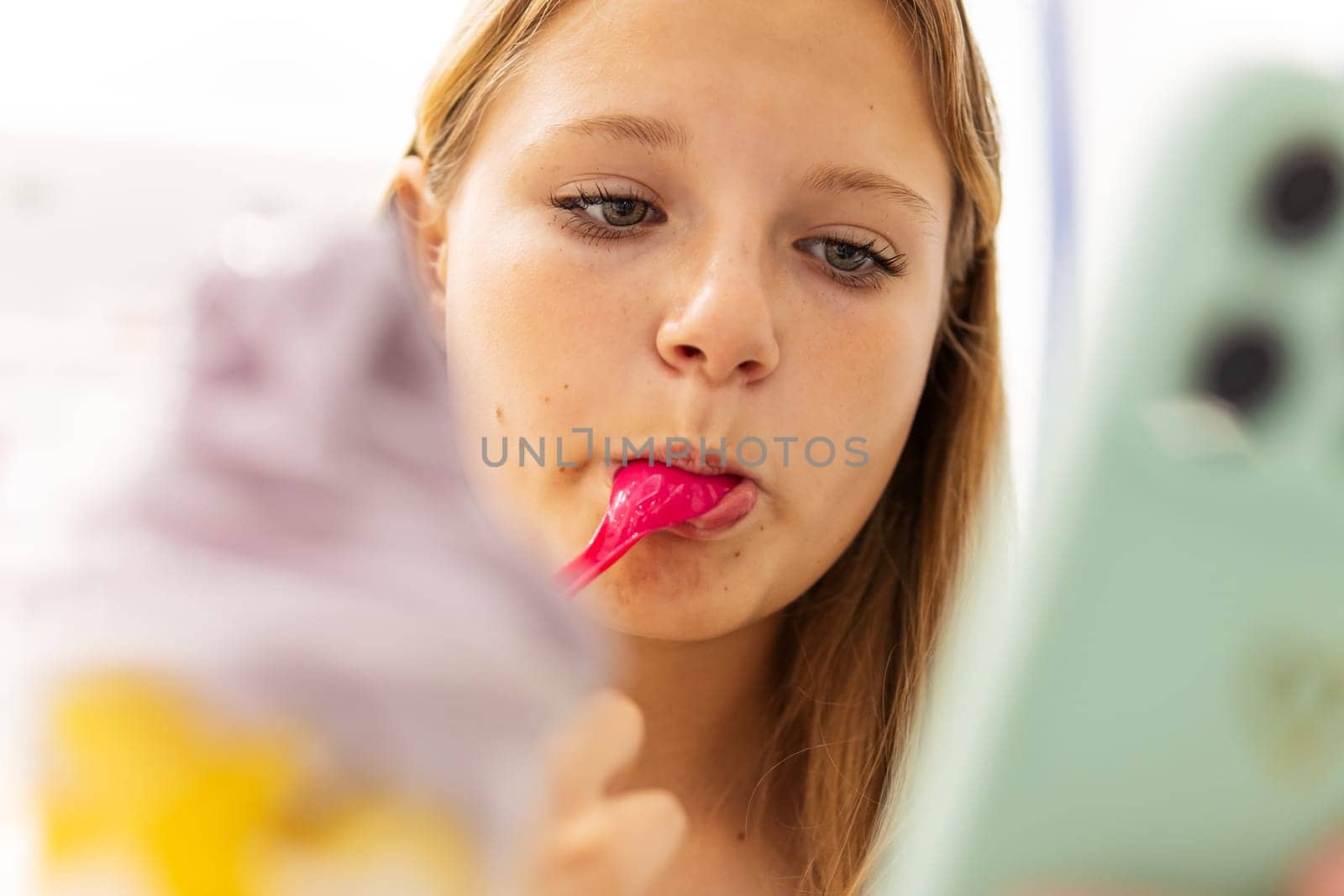 Young blonde woman eating ice cream and message on phone sitting in cafe. High quality photo