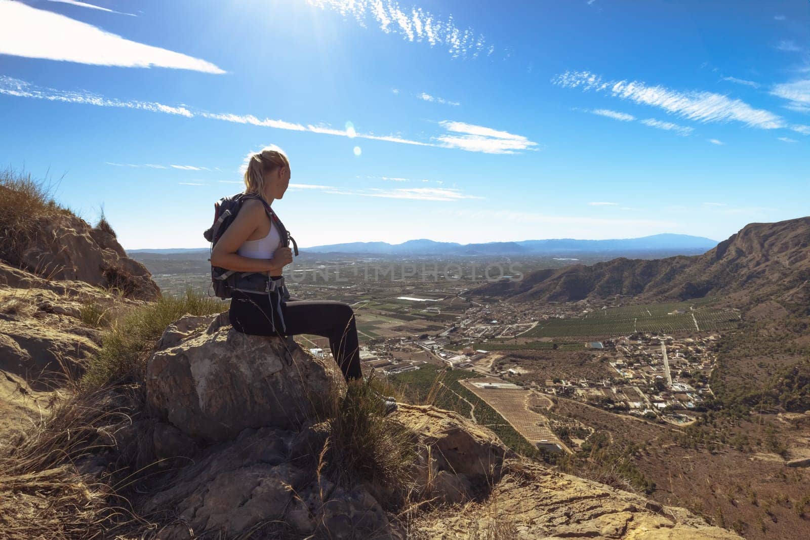 a girl in sportswear with a backpack sits on the mountain admiring the views. Hiking concept by PopOff