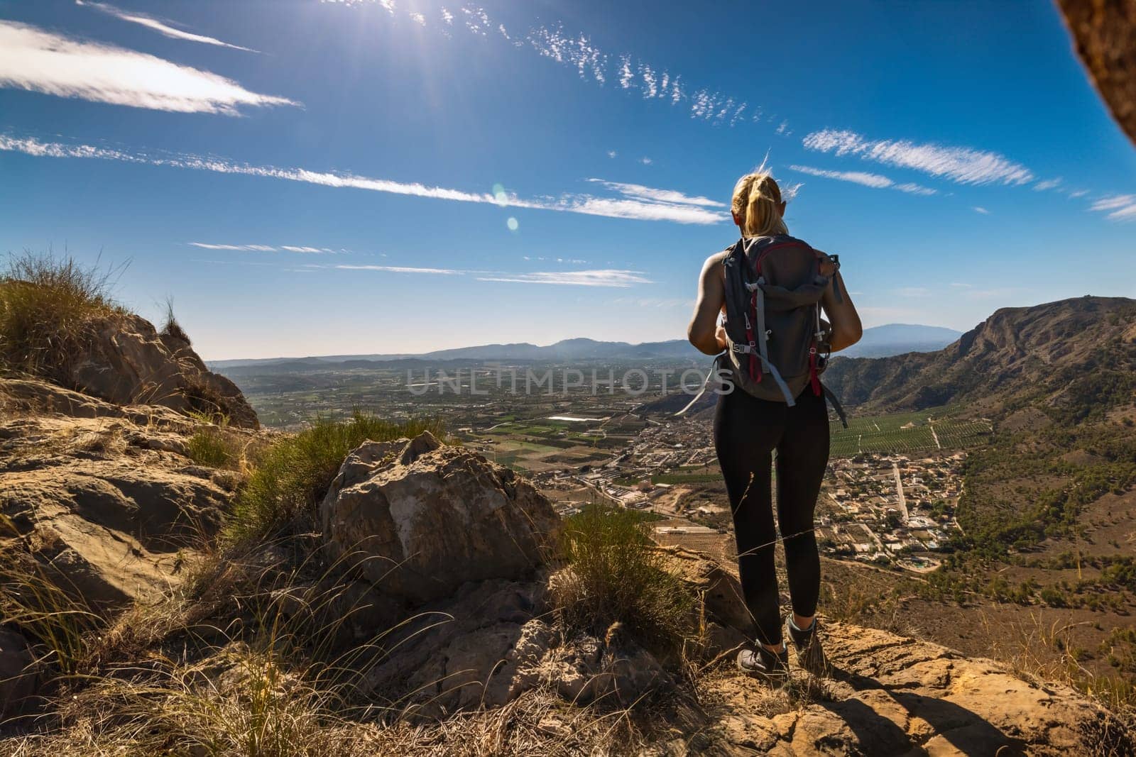 Hiker with backpack standing on top of the mountain and enjoying valley view at sunrise by PopOff