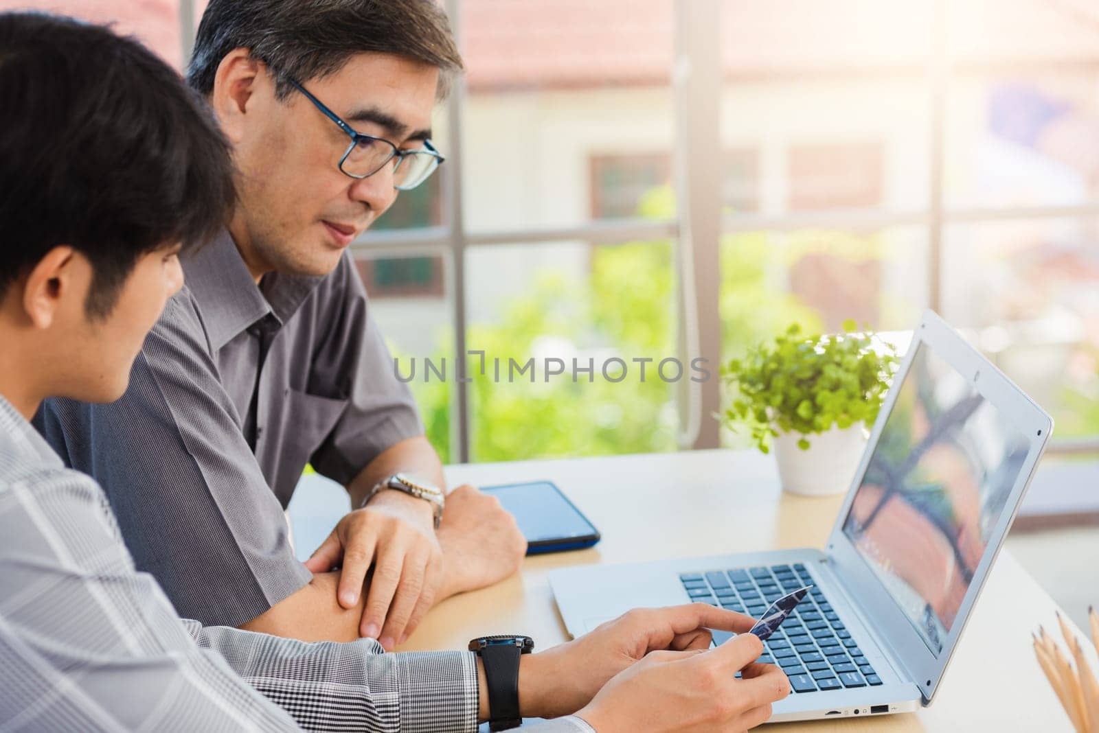 young man teaching senior father how to use credit card for shopping online with laptop computer by Sorapop