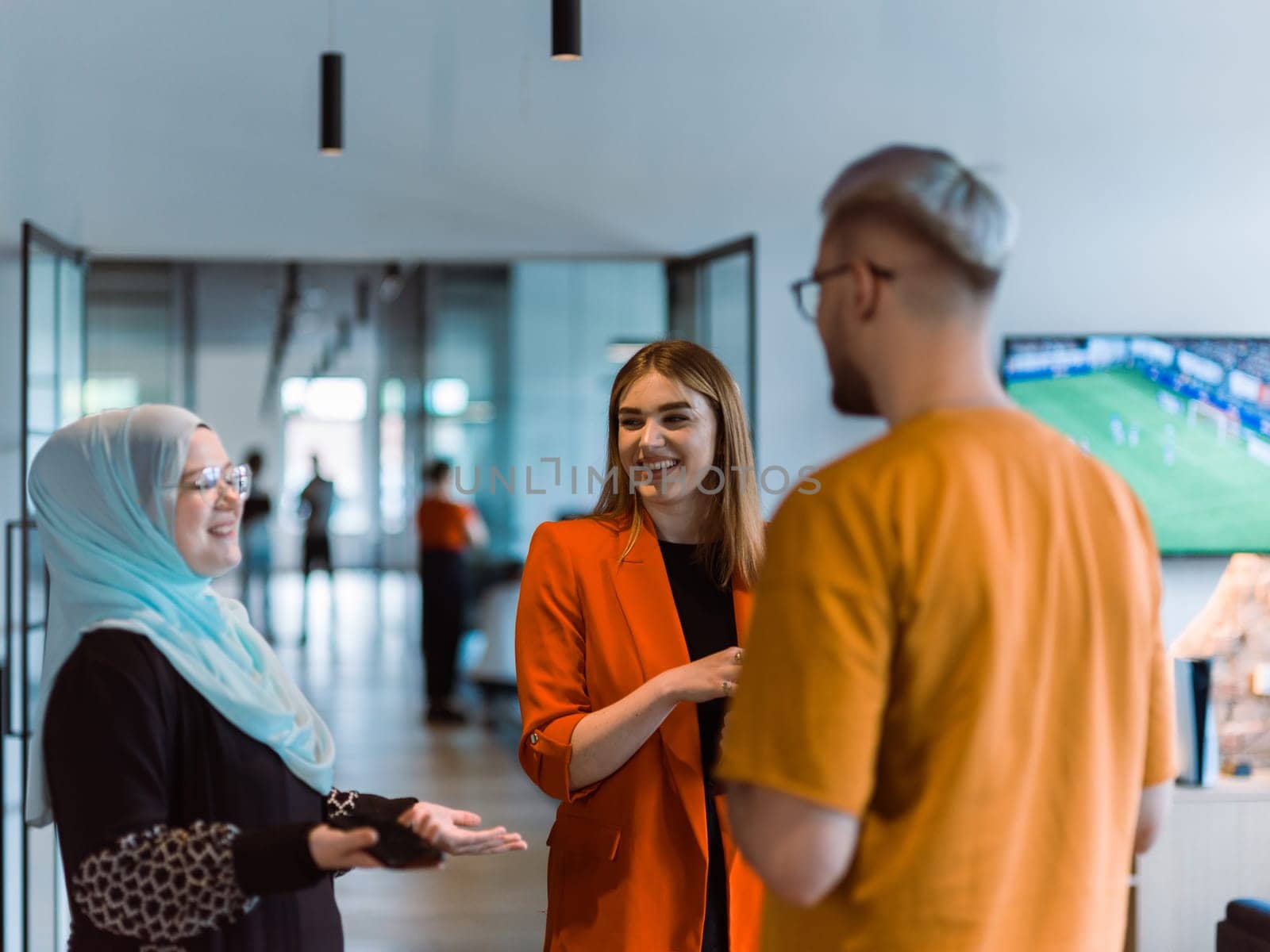 A group of young business colleagues, including a woman in a hijab, stands united in the modern corridor of a spacious startup coworking center, representing diversity and collaborative spirit by dotshock