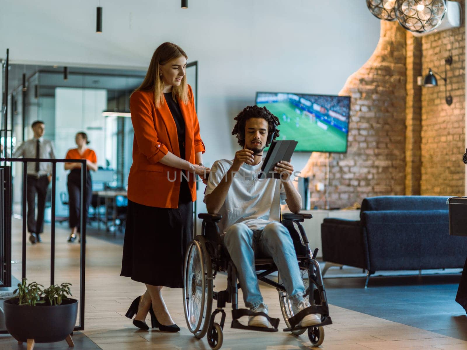 African-American businessman in a wheelchair engages in a collaborative discussion, using a tablet, with his business colleague, exemplifying the seamless integration of adaptive technology and fostering diversity in a modern corporate environment.
